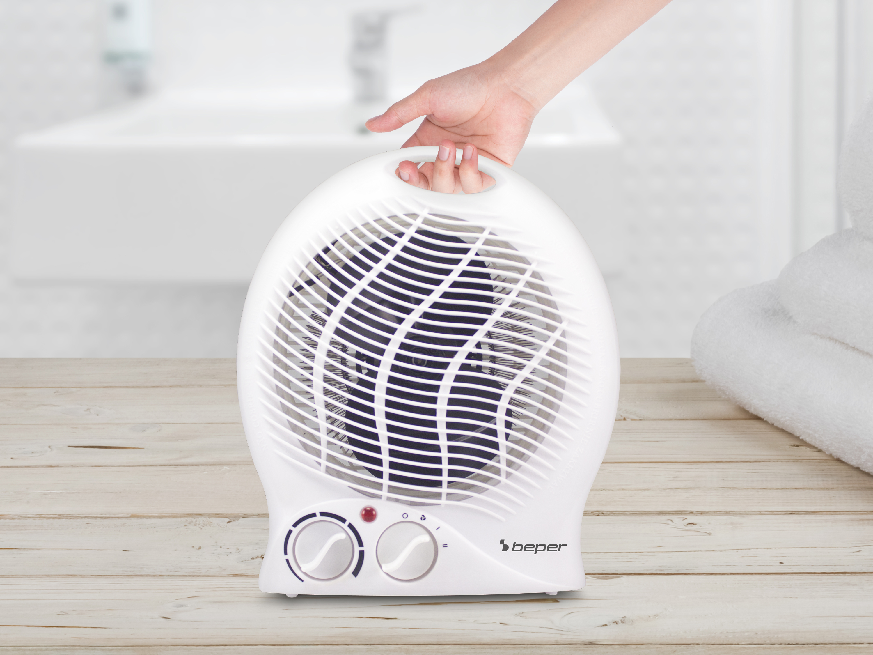 Un ventilatore bianco con maniglia è su un tavolo di legno. Una mano tiene la maniglia. Accanto c'è un asciugamano.