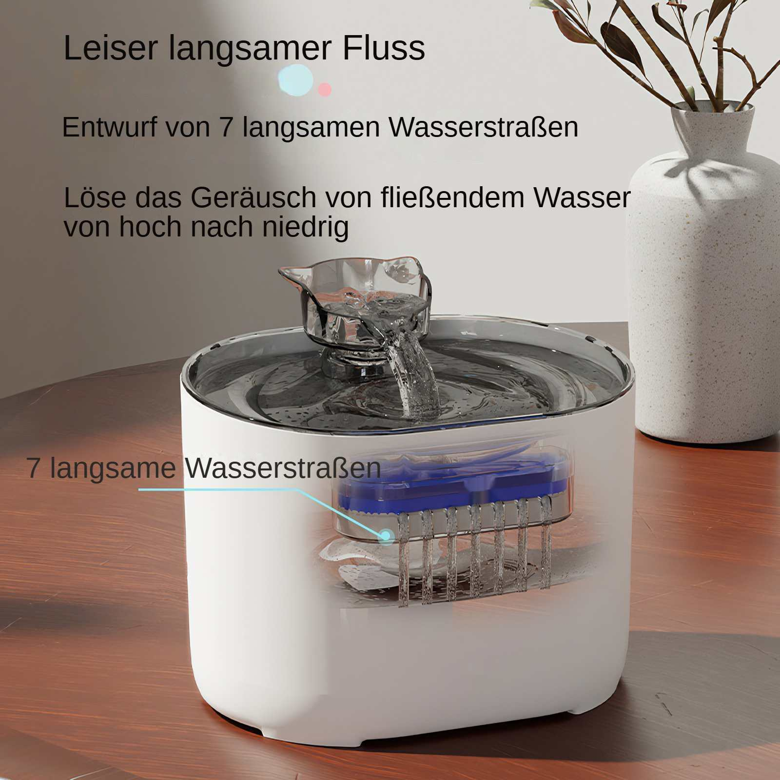 Ein Wasserbrunnen mit sichtbarem Wasserfluss. Der Brunnen ist weiß und hat blaue und silberne Teile. Im Hintergrund steht eine Vase.