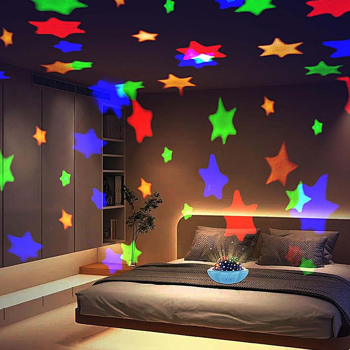Ein Schlafzimmer mit Bett und Sternenprojektor. Farbige Sterne werden an Decke und Wänden projiziert. Das Bett hat Kissen und eine Decke.