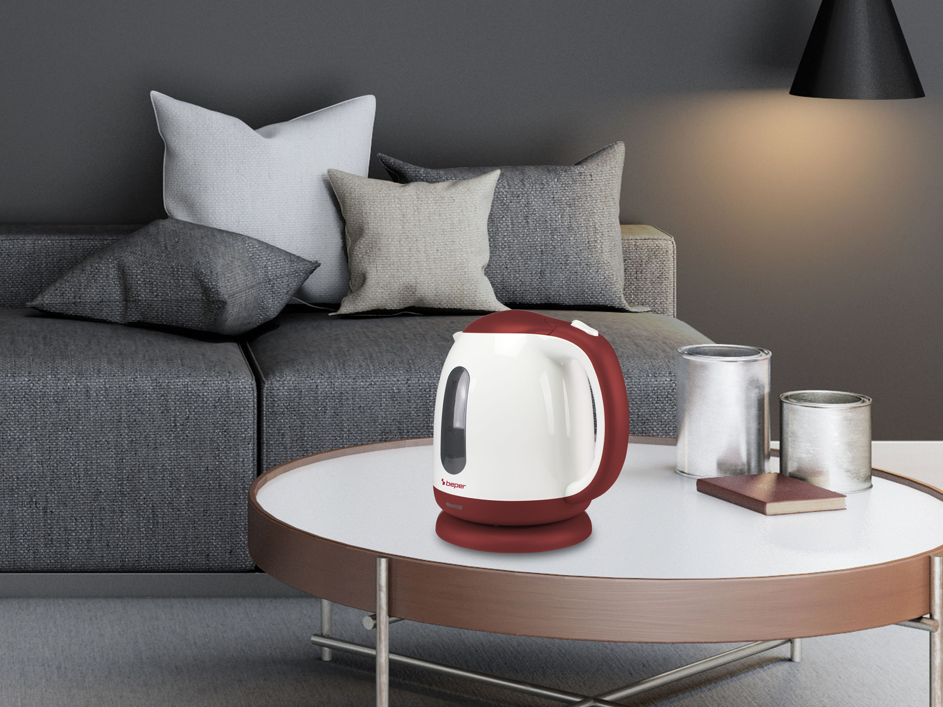 Un bollitore elettrico rosso e bianco su un tavolo rotondo. Un divano grigio con cuscini sullo sfondo.