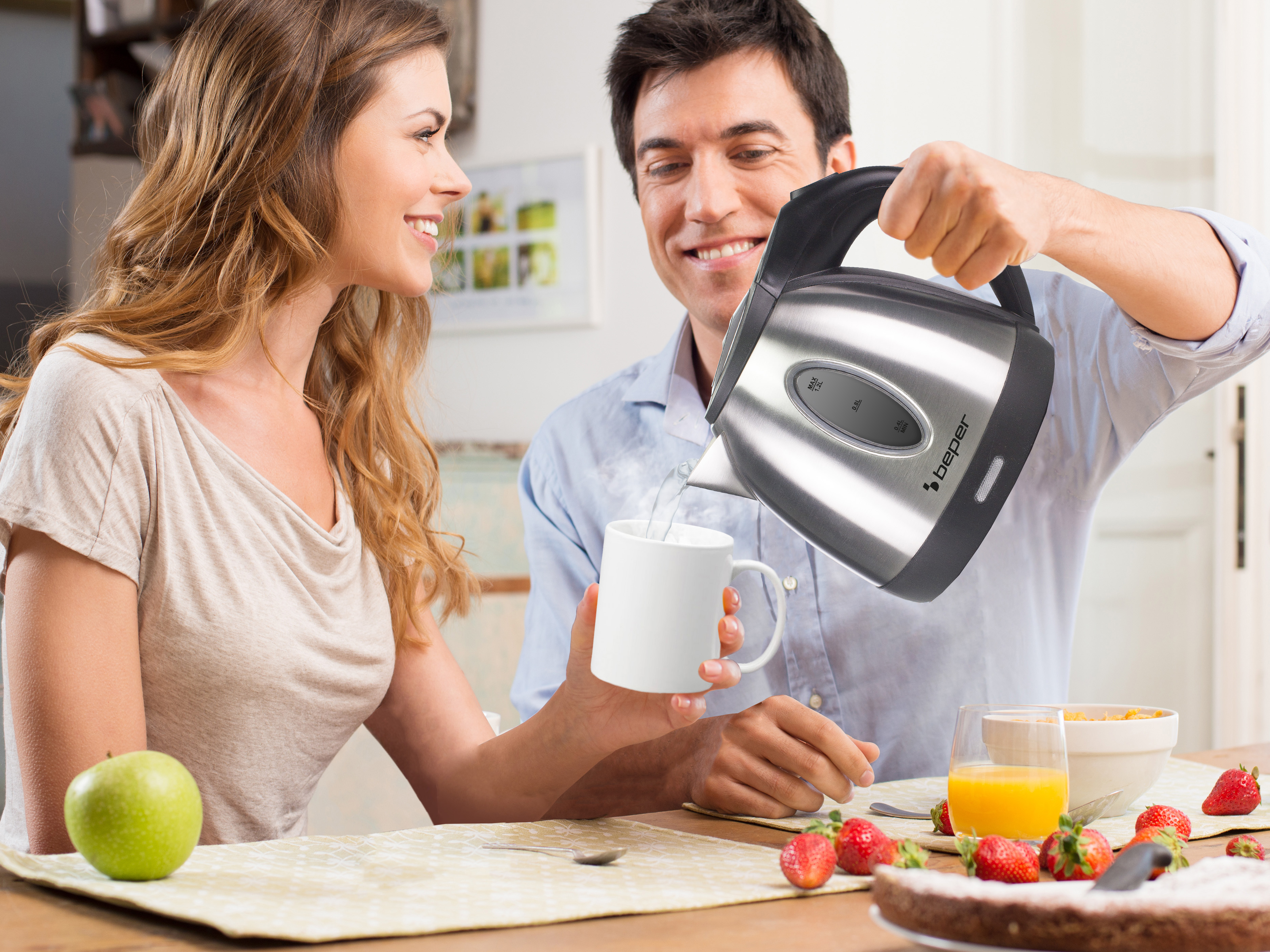 Un uomo versa l'acqua da un bollitore in una tazza. Una donna gli sorride. Sul tavolo ci sono cibi per la colazione.