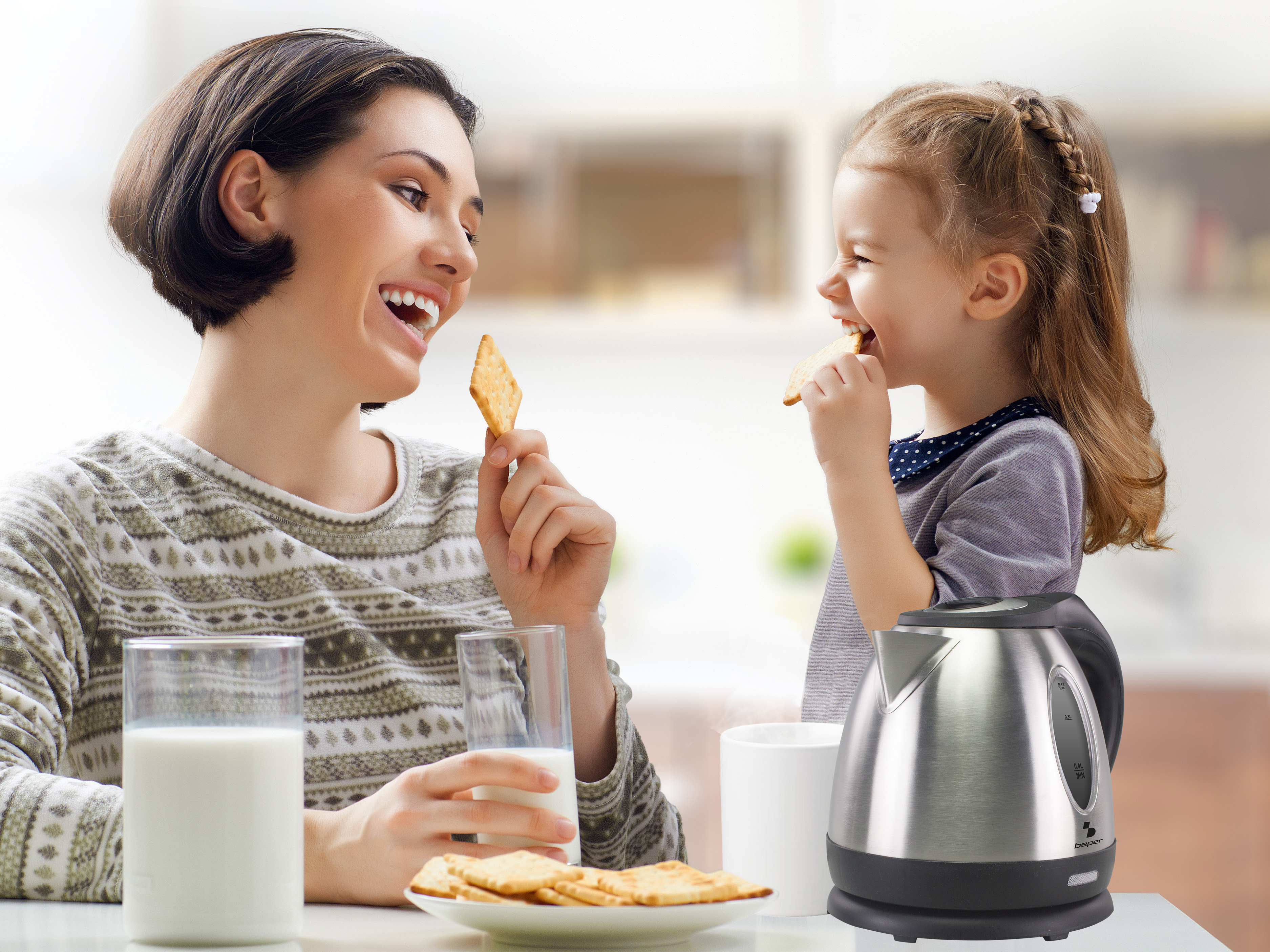 Una donna e una bambina mangiano cracker. Un bicchiere di latte e un bollitore sono sul tavolo. Sorridono e ridono.