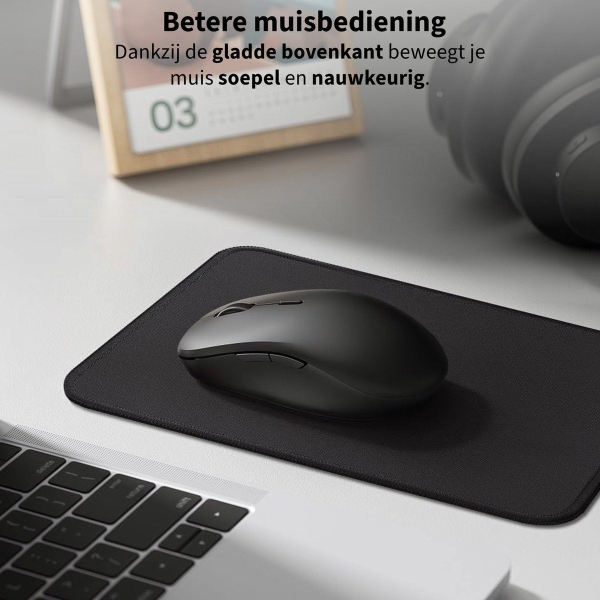 A black mouse on a black mousepad, a keyboard in the corner, and a calendar in the background. Text in Dutch is present.