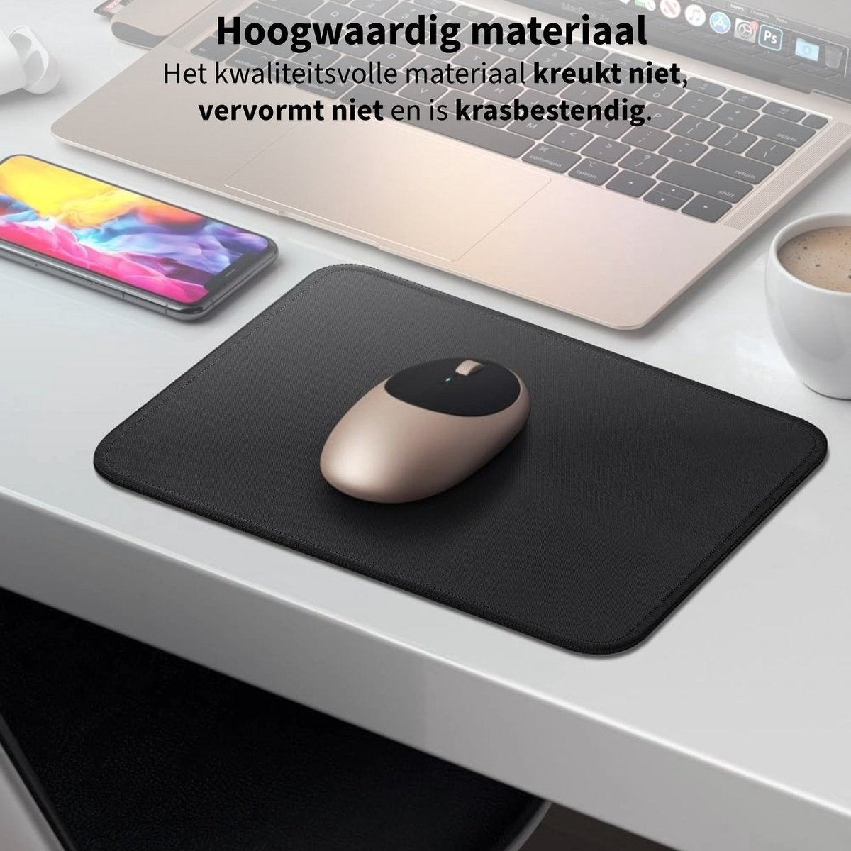 A black mousepad with a gold mouse on a white desk. A laptop and a phone are also on the desk. A cup of coffee is on the right.