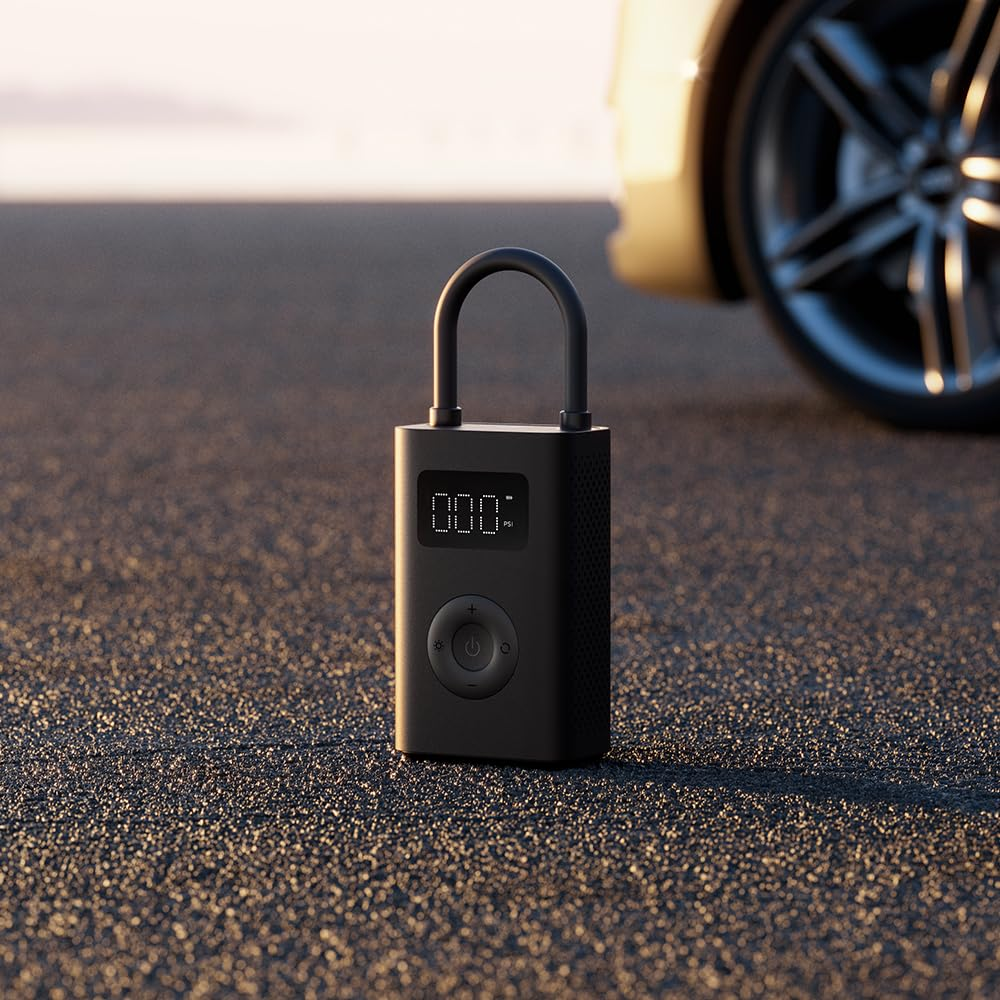 Ein schwarzer Reifenfüller steht auf Asphalt, in der Nähe eines gelben Autoreifens. Das Display des Füllers zeigt '0,00'.