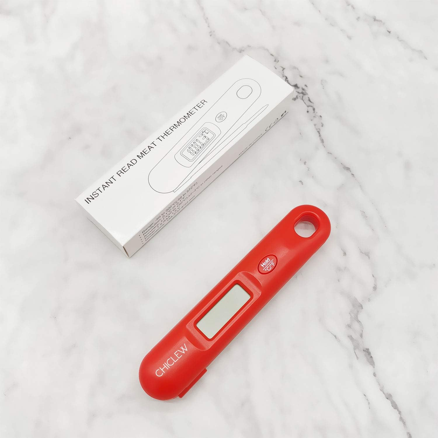 Ein rotes Fleischthermometer liegt neben seiner weißen Schachtel. Das Thermometer hat einen Bildschirm und die Schachtel sagt 'Instant Read Meat Thermometer'.