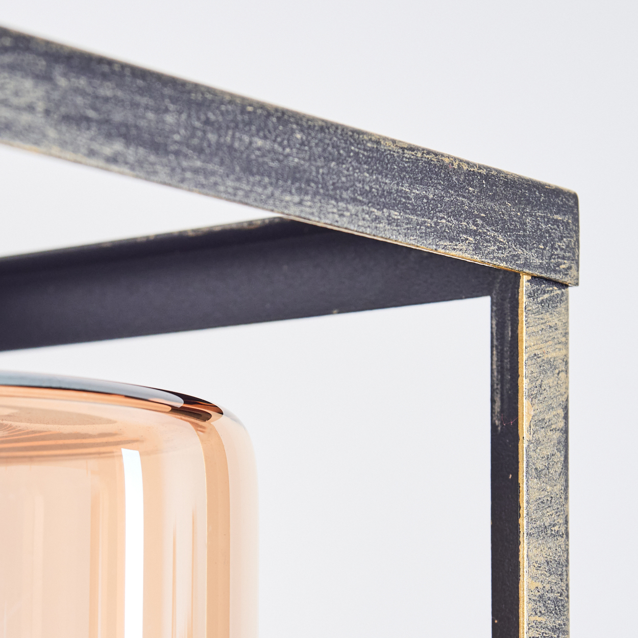 Nahaufnahme eines dekorativen Metallrahmens mit einem zylindrischen, bernsteinfarbenen Glasbehälter. Der Rahmen hat ein Used-Finish.