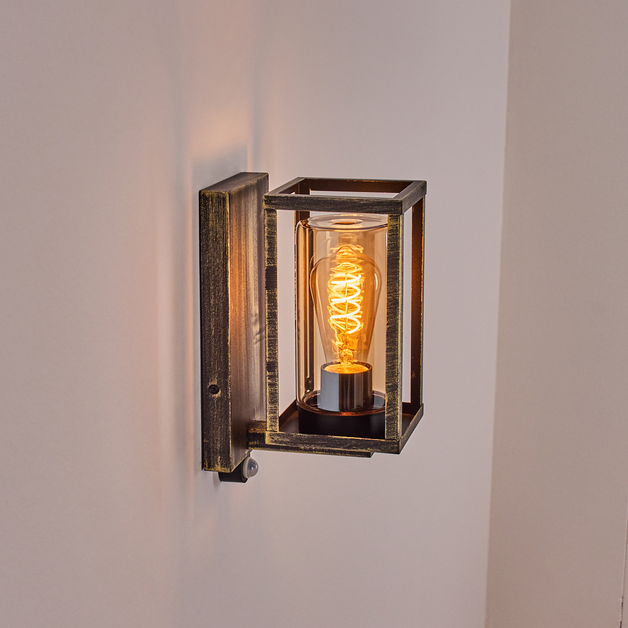 Eine Wandleuchte im Vintage-Design. Sie hat einen rechteckigen Rahmen um einen zylindrischen Glaskörper mit Edison-Glühbirne.
