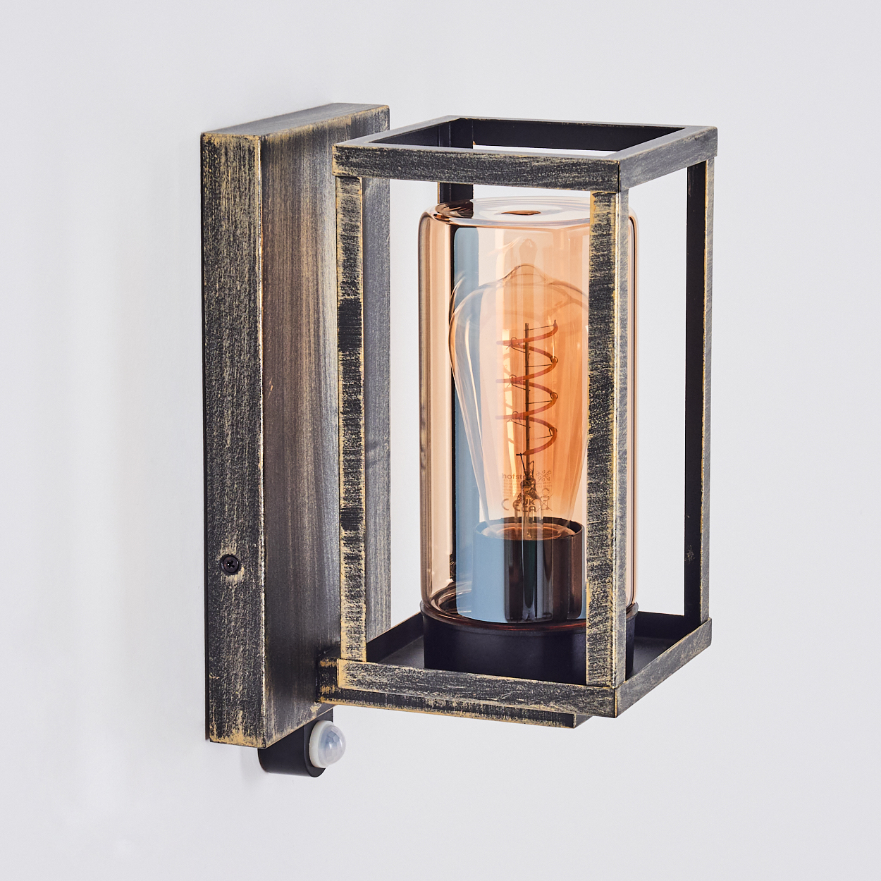 Eine Wandlampe mit Käfigdesign. Die Lampe hat eine warmtonige Glühbirne in einem Glaszylinder. Der Rahmen ist schwarz und goldfarben.