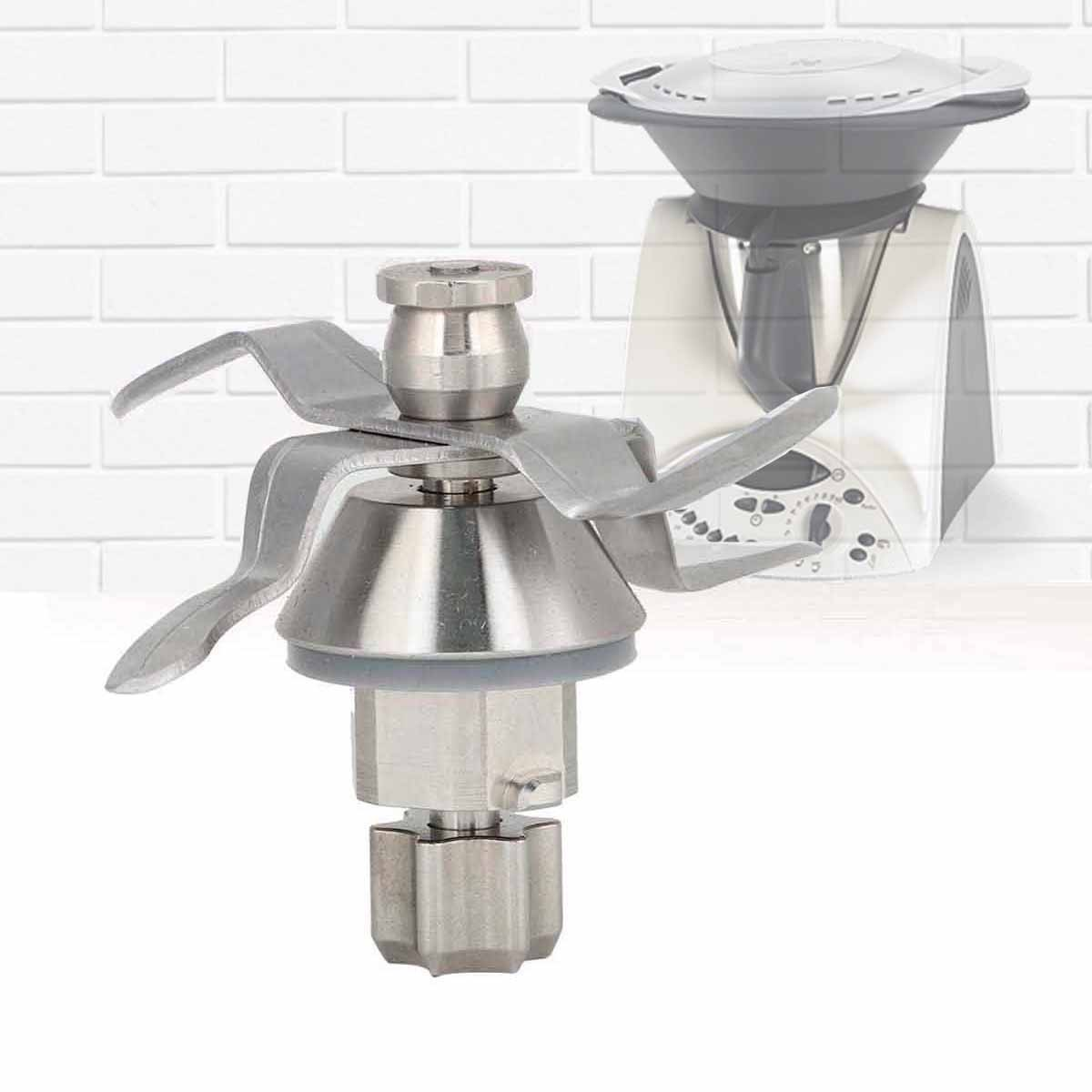 Un conjunto de cuchillas de licuadora de acero inoxidable está enfocado. Un electrodoméstico de cocina blanco y gris está borroso en el fondo.