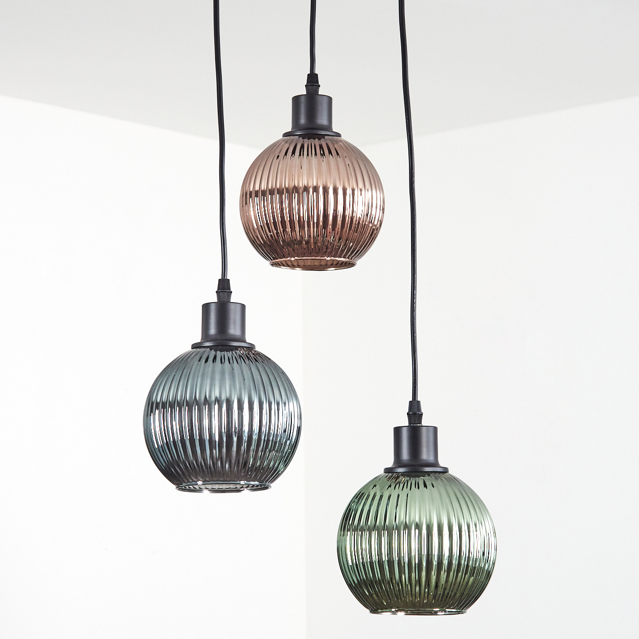 Drei Pendelleuchten mit gerippten Glasschirmen in Bronze, Türkis und Grün hängen an schwarzen Kabeln vor weißem Hintergrund.