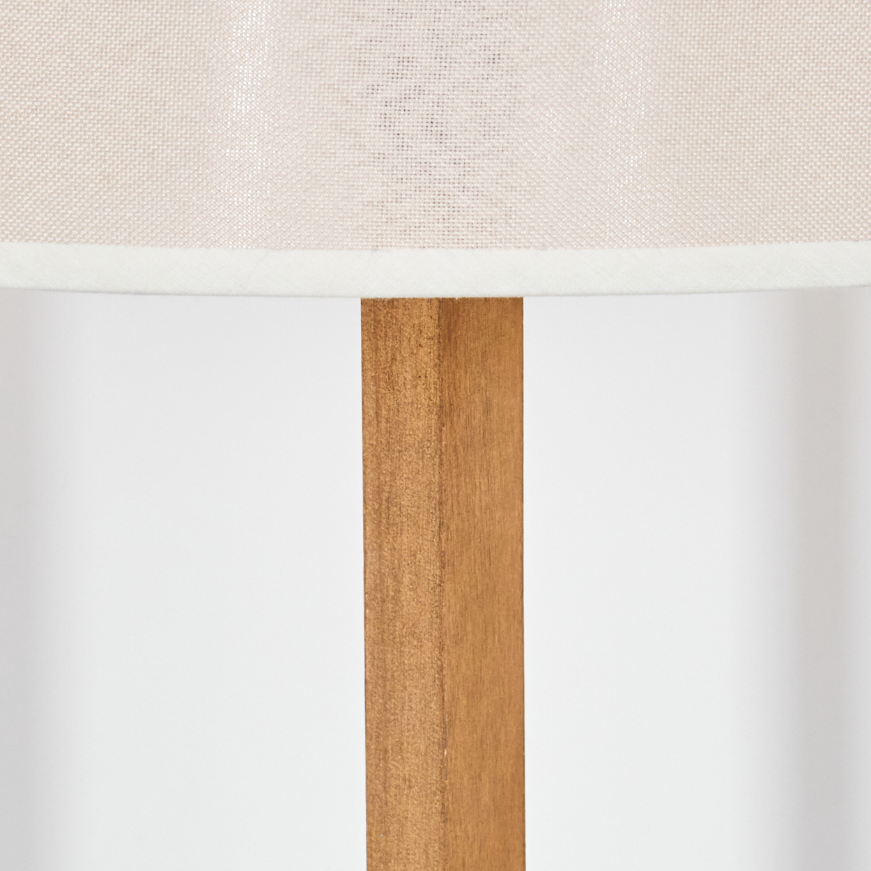 Nahaufnahme einer Lampe. Ein beiger Lampenschirm sitzt über einem Holzständer. Der Hintergrund ist weiß.