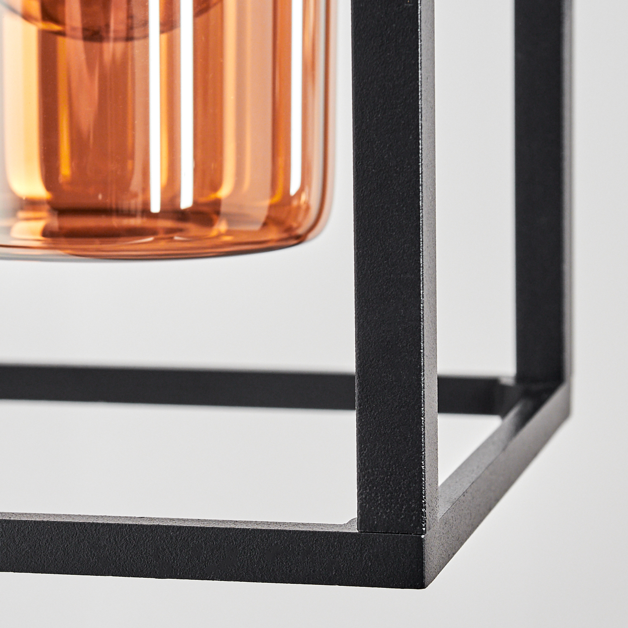 Nahaufnahme eines Dekorationsobjekts. Es hat einen schwarzen Metallrahmen und einen Glaszylinder mit orangefarbenem Farbton. Weißer Hintergrund.
