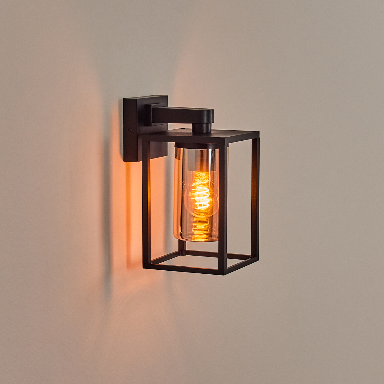 Eine schwarze, moderne Wandleuchte mit einer glühenden Glühbirne in einem Glaskylinder, montiert an einer beigefarbenen Wand.