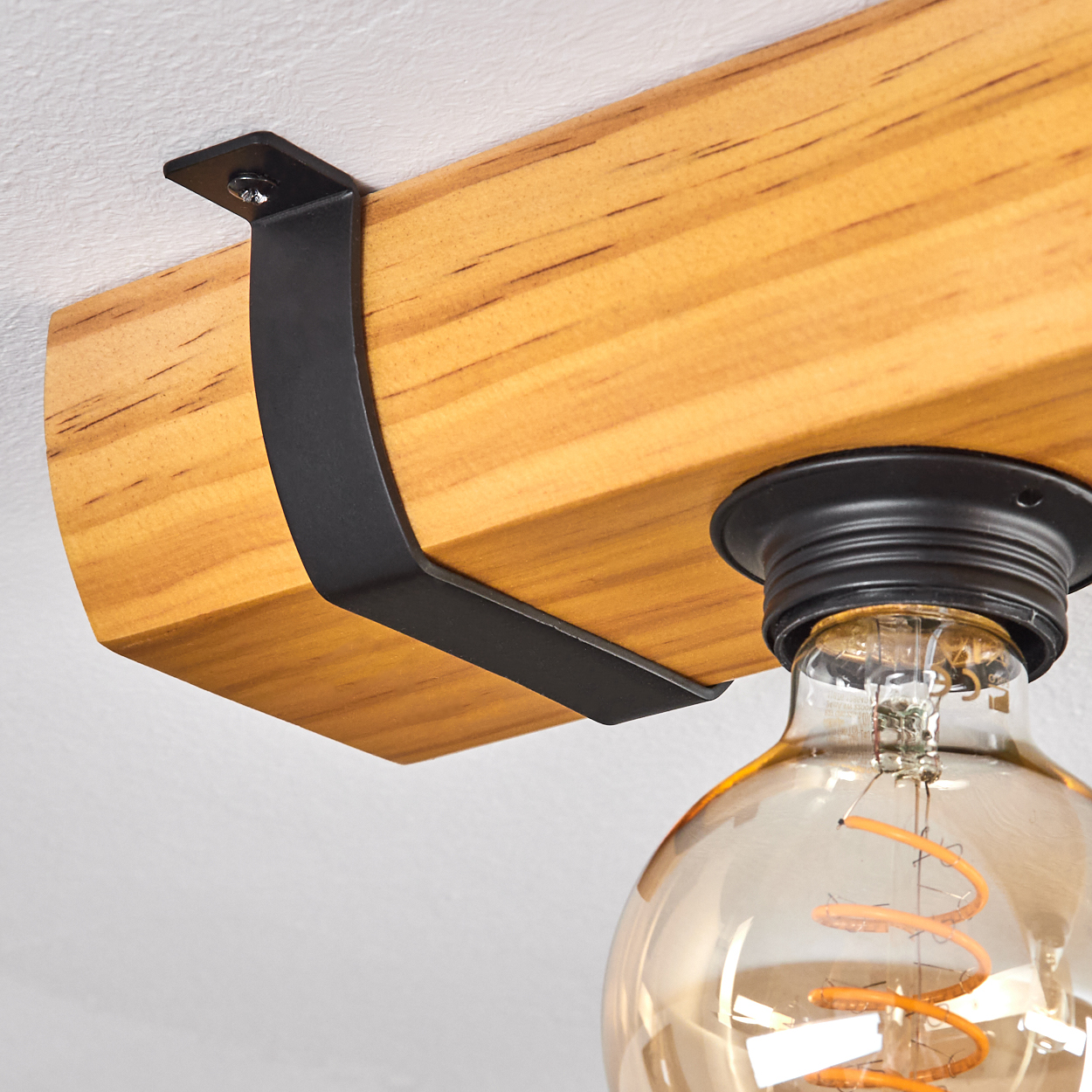 Holzbalken mit schwarzem Metallträger und einer freiliegenden Glühbirnen-Leuchte. Die Glühbirne hat einen orangefarbenen Glühfaden.