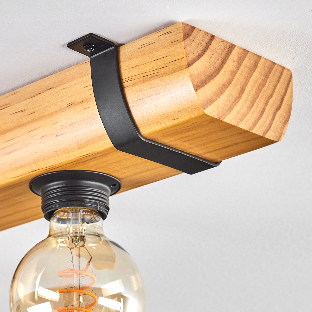 Ein Holzbalken mit einer schwarzen Metallhalterung und einer hängenden Glühbirne. Die Glühbirne ist aus Glas und leuchtet.