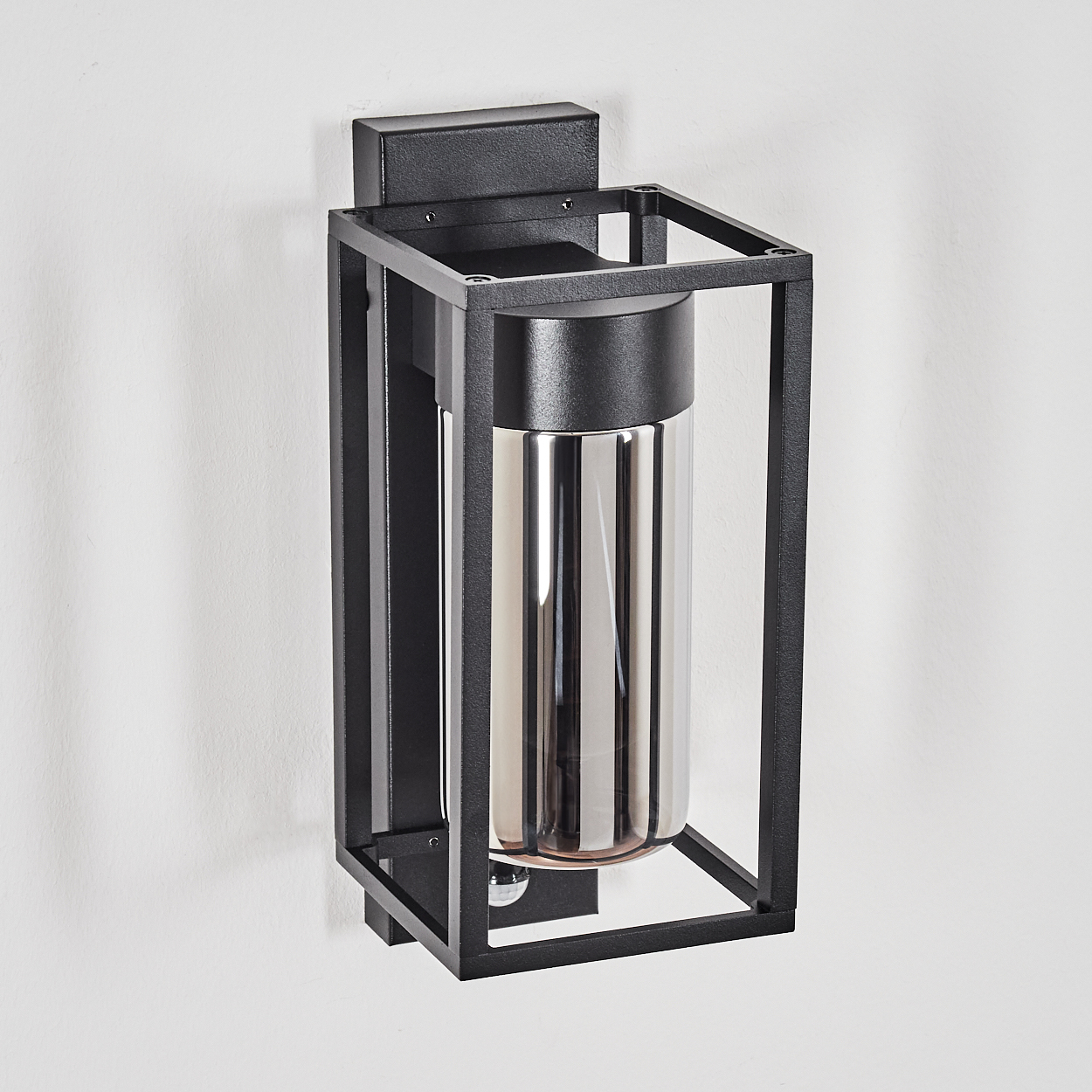 Eine schwarze Außenwandleuchte. Sie hat einen rechteckigen Käfig um eine zylindrische Leuchte mit reflektierender Oberfläche.