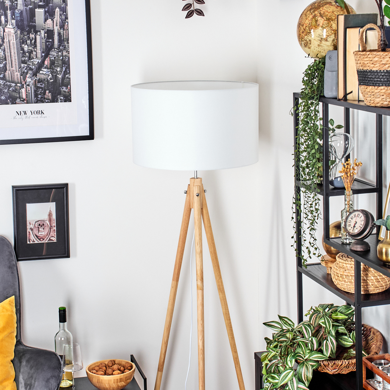 Ein Raum mit einer weißen Lampe, Holzbeinen und einem weißen Lampenschirm. Es gibt Regale mit Pflanzen und Dekorationen. Ein Bild von New York hängt an der Wand.