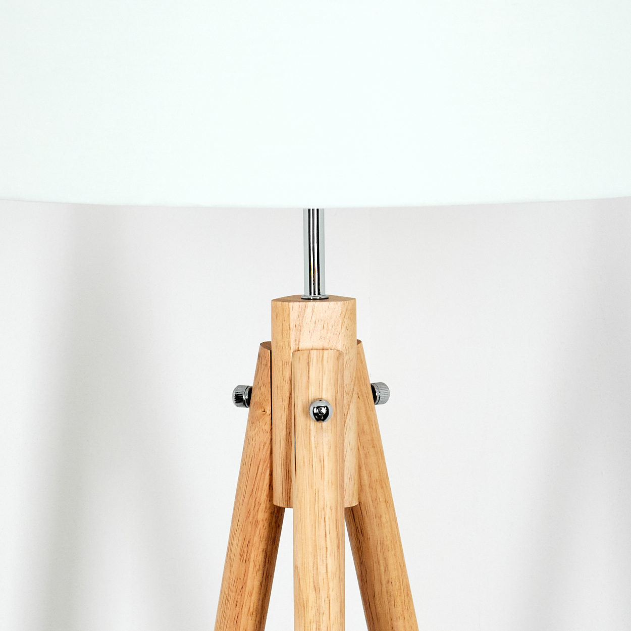 Eine Holzstativlampe mit weißem Lampenschirm. Das Stativ besteht aus hellem Holz, der Hintergrund ist schlicht weiß.
