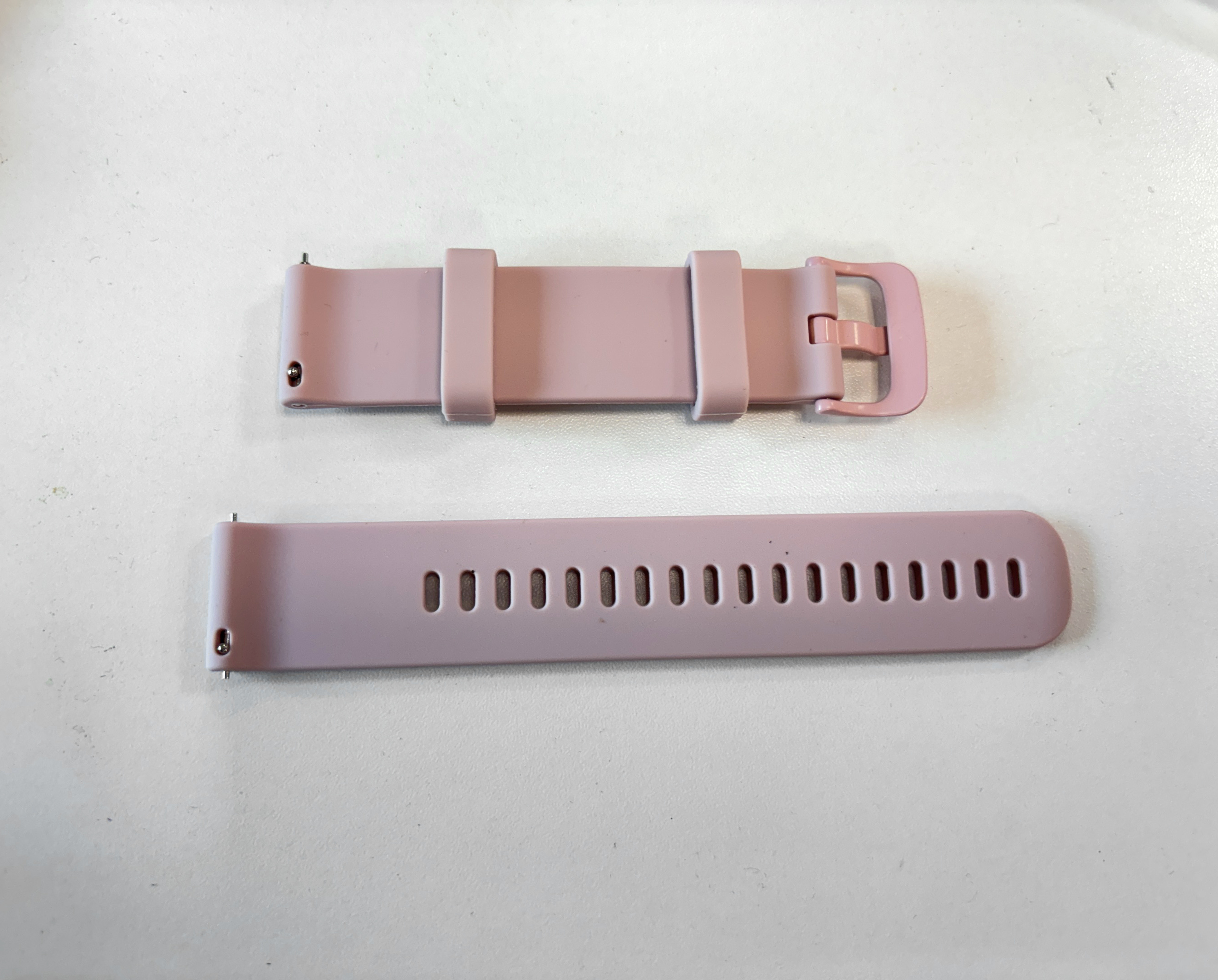 Zwei rosa Uhrenarmbänder auf einer weißen Oberfläche. Eines hat eine Schnalle. Das andere hat Löcher.