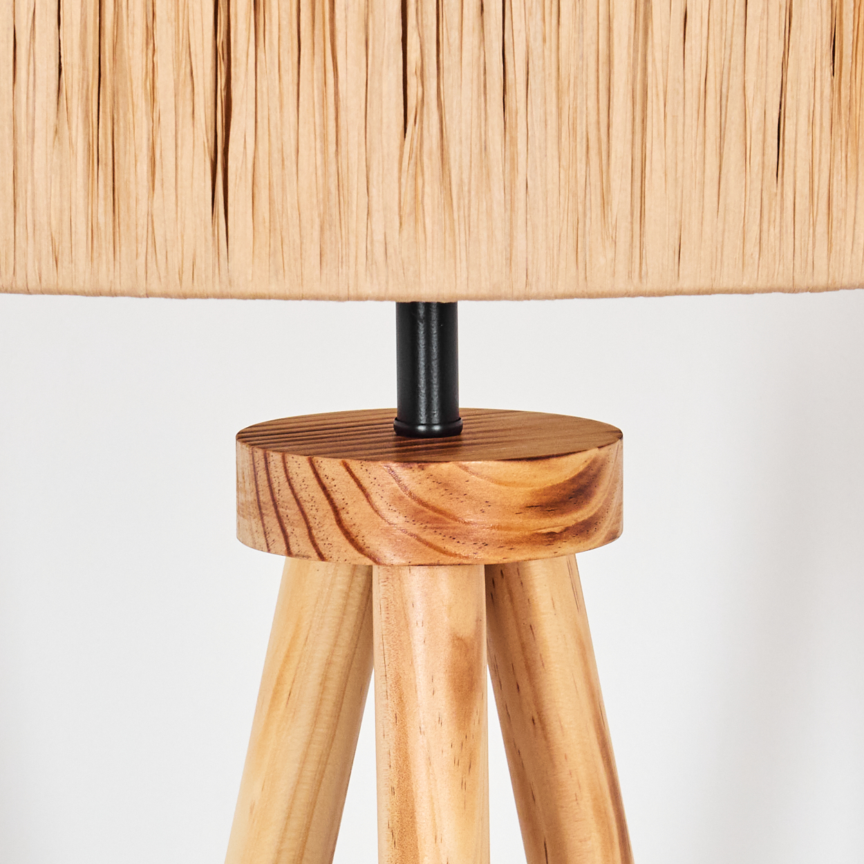 Ein beigefarbener Lampenschirm sitzt auf einem Holzsockel mit drei Beinen. Eine schwarze Metallstange verbindet Schirm und Sockel. Weißer Hintergrund.
