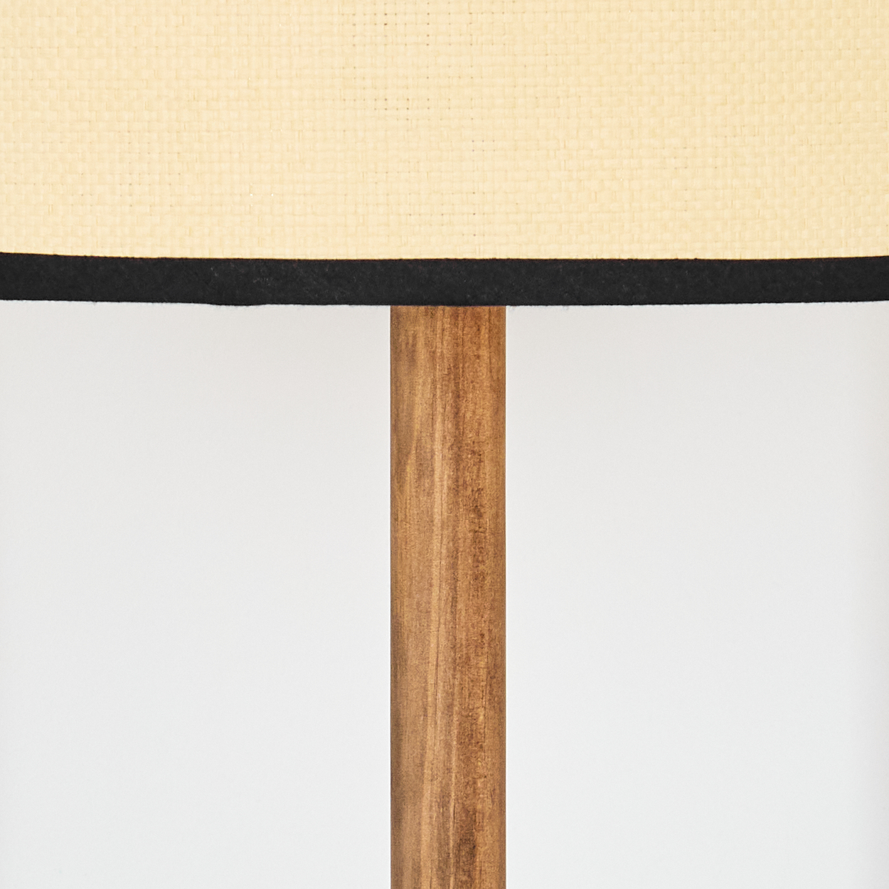 Nahaufnahme einer Lampe. Beigefarbener Lampenschirm mit schwarzer Einfassung, Holzpfahl und weißem Hintergrund.