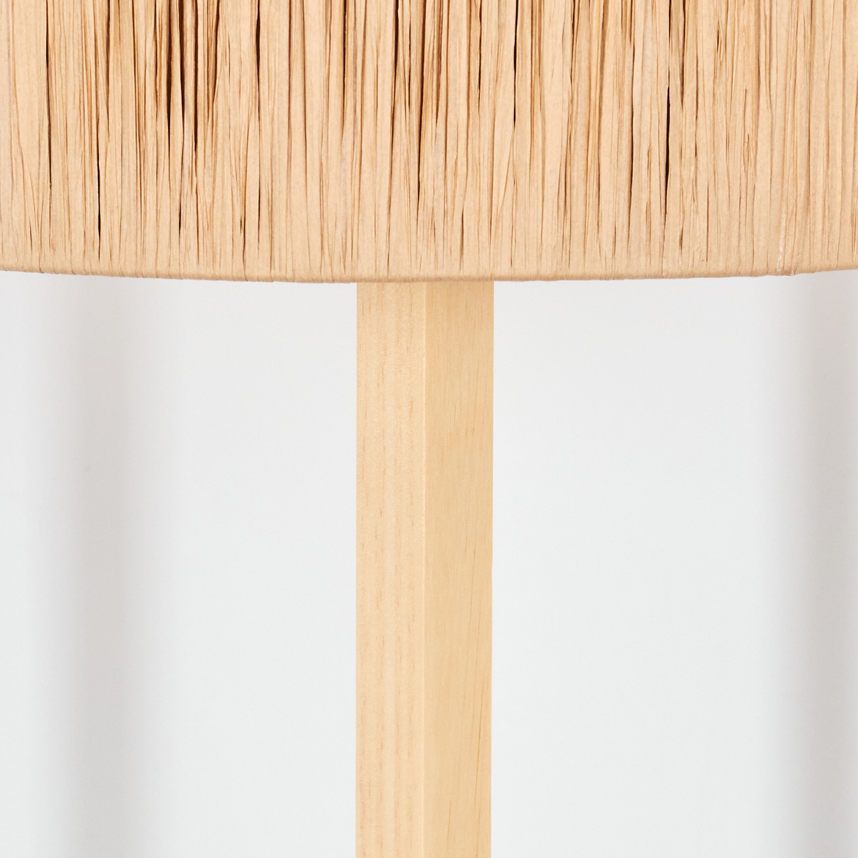 Eine Lampe mit hellbraunem Schirm aus vertikalen Streifen, getragen von einem hellen Holzpfosten auf weißem Grund.