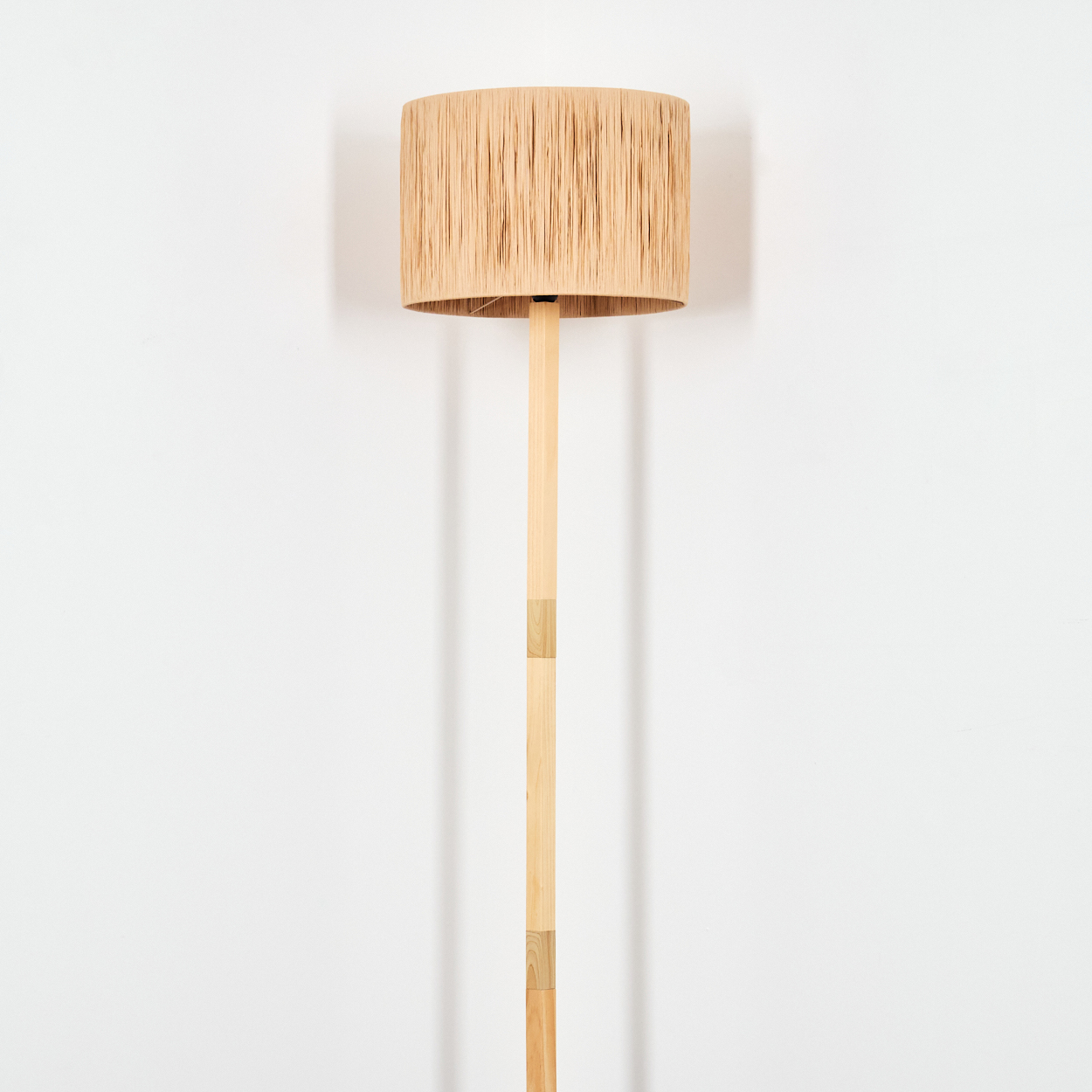 Ein beiger Lampenschirm sitzt auf einem Holzpfahl. Die Lampe ist vor einem weißen Hintergrund zentriert.