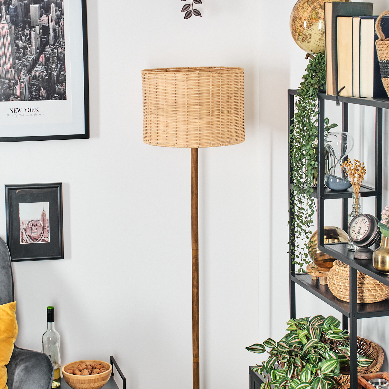 Ein Raum mit einer Stehlampe und Regalen. Die Lampe hat einen Korbschirm. Regale enthalten Pflanzen, Bücher und Dekorationsartikel.