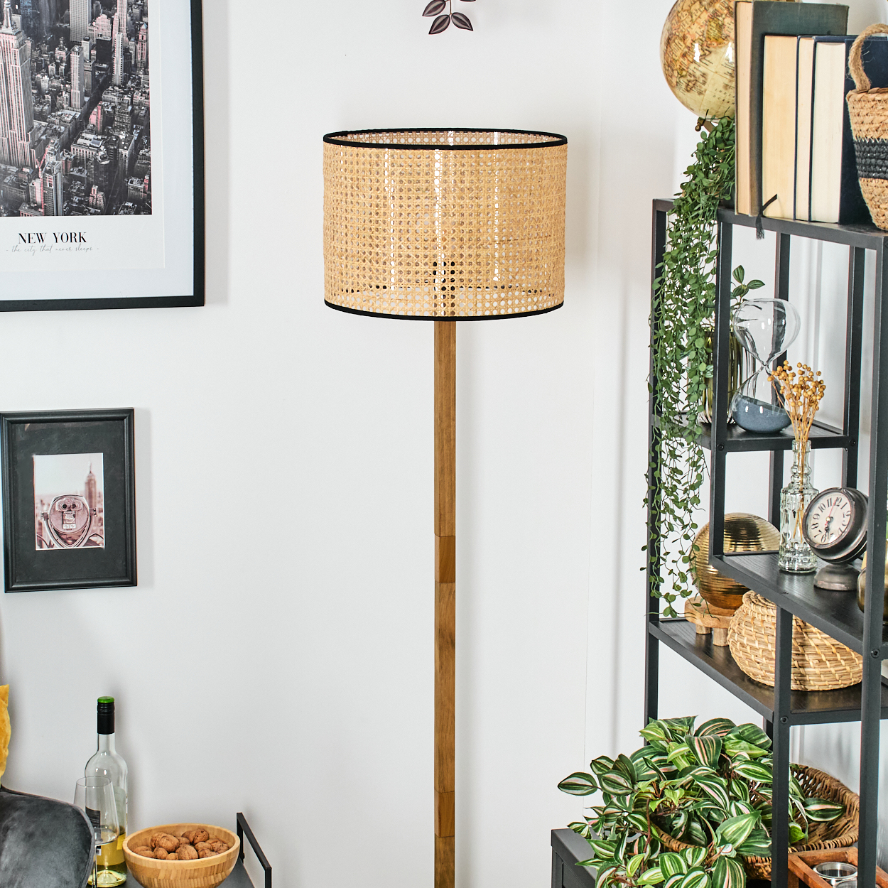 Eine gewebte Lampe steht in einem Raum. Regale rechts sind mit Dekor gefüllt. Es gibt einen New York-Druck und andere gerahmte Fotos.