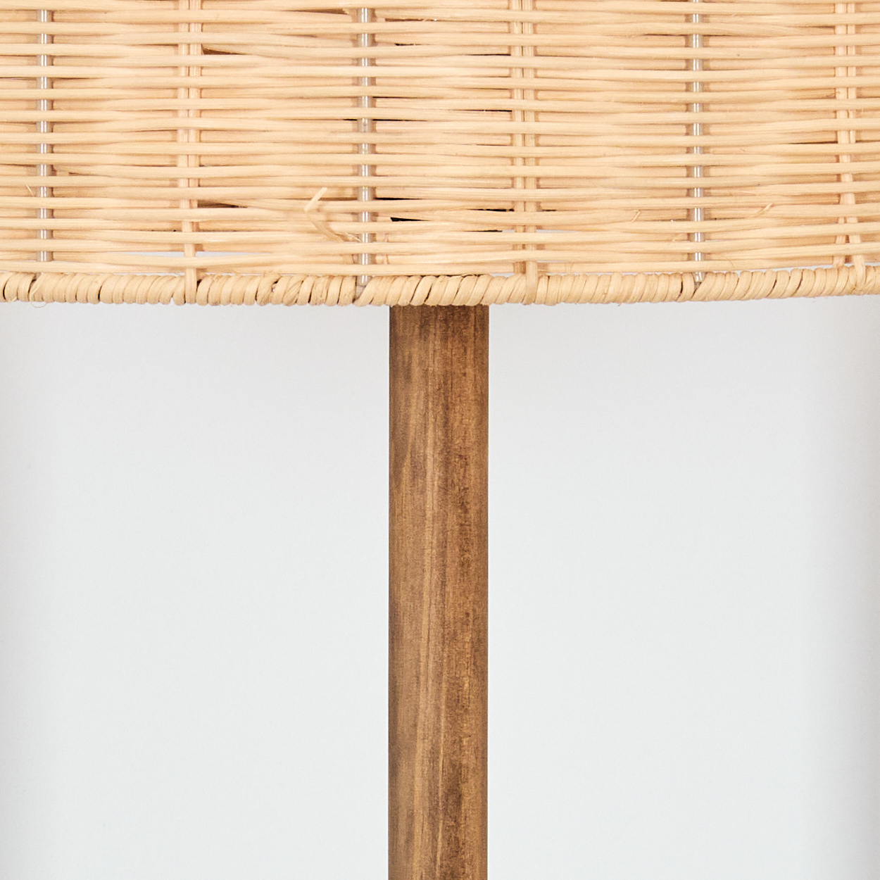 Nahaufnahme einer Lampe. Gewebter Korbflechtschirm über einem braunen Holzpfosten. Der Hintergrund ist eine schlichte weiße Wand.