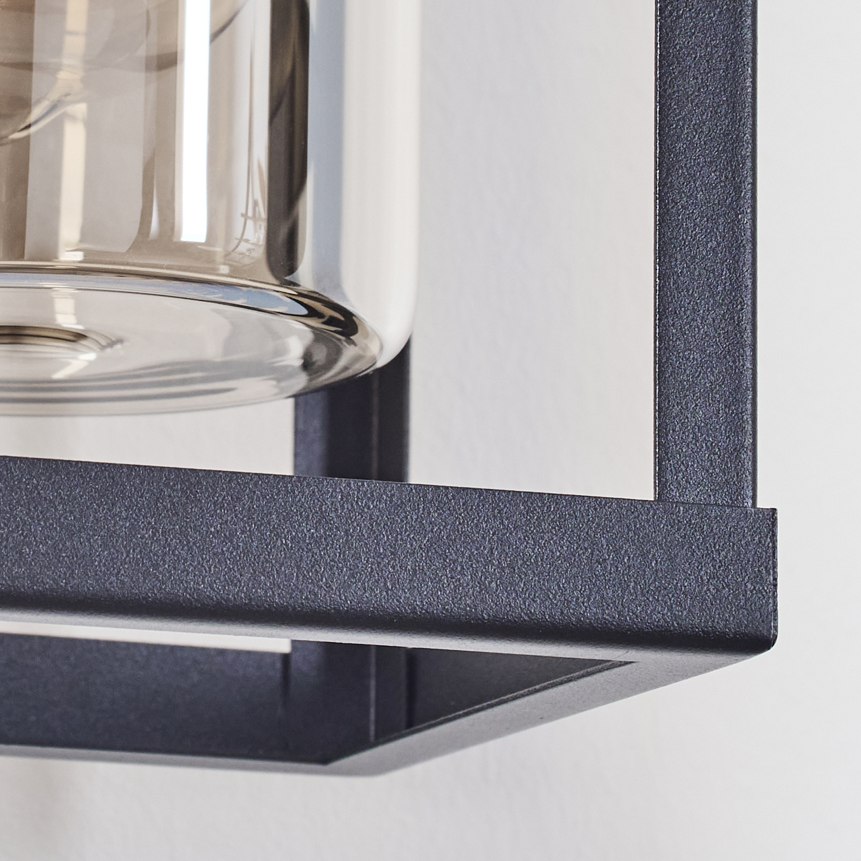 Nahaufnahme einer modernen Lampe. Sie hat einen durchsichtigen Glasschirm in einem schwarzen Metallrahmen vor einer weißen Wand.
