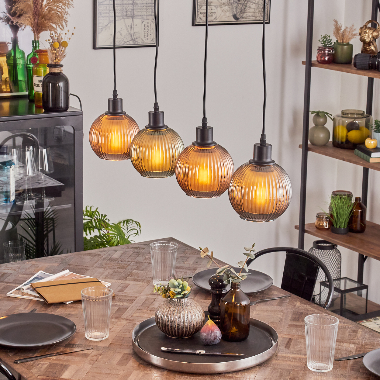 Esszimmer-Setup mit Pendelleuchten, einem Holztisch und dekorativen Gegenständen. Enthält Teller, Gläser und ein Tablett mit Deko.