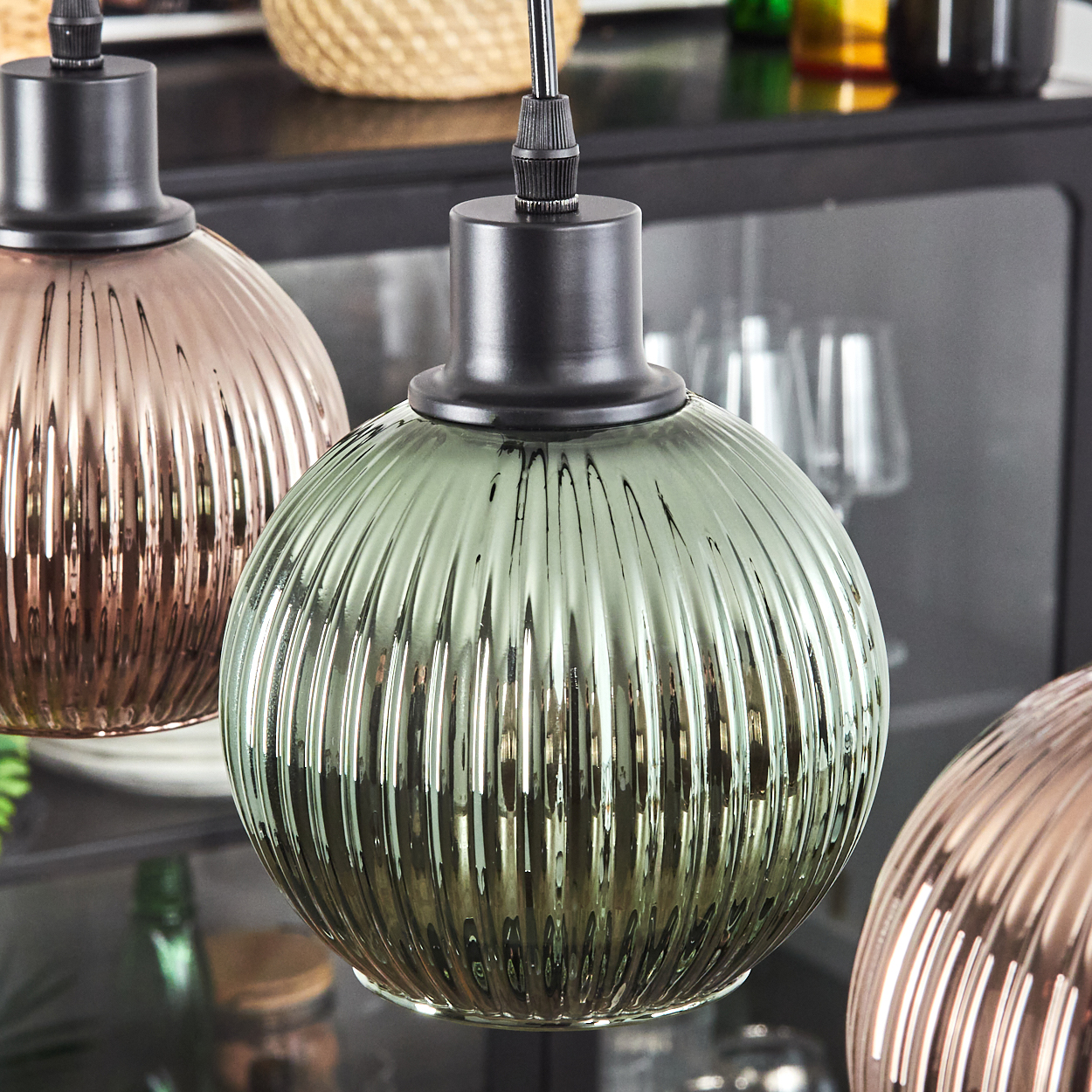 Drei Pendelleuchten aus Glas, geripptes Design, in Grün-, Rosé- und Bronzetönen. Schwarze Halterungen und Hintergrund mit Korb.