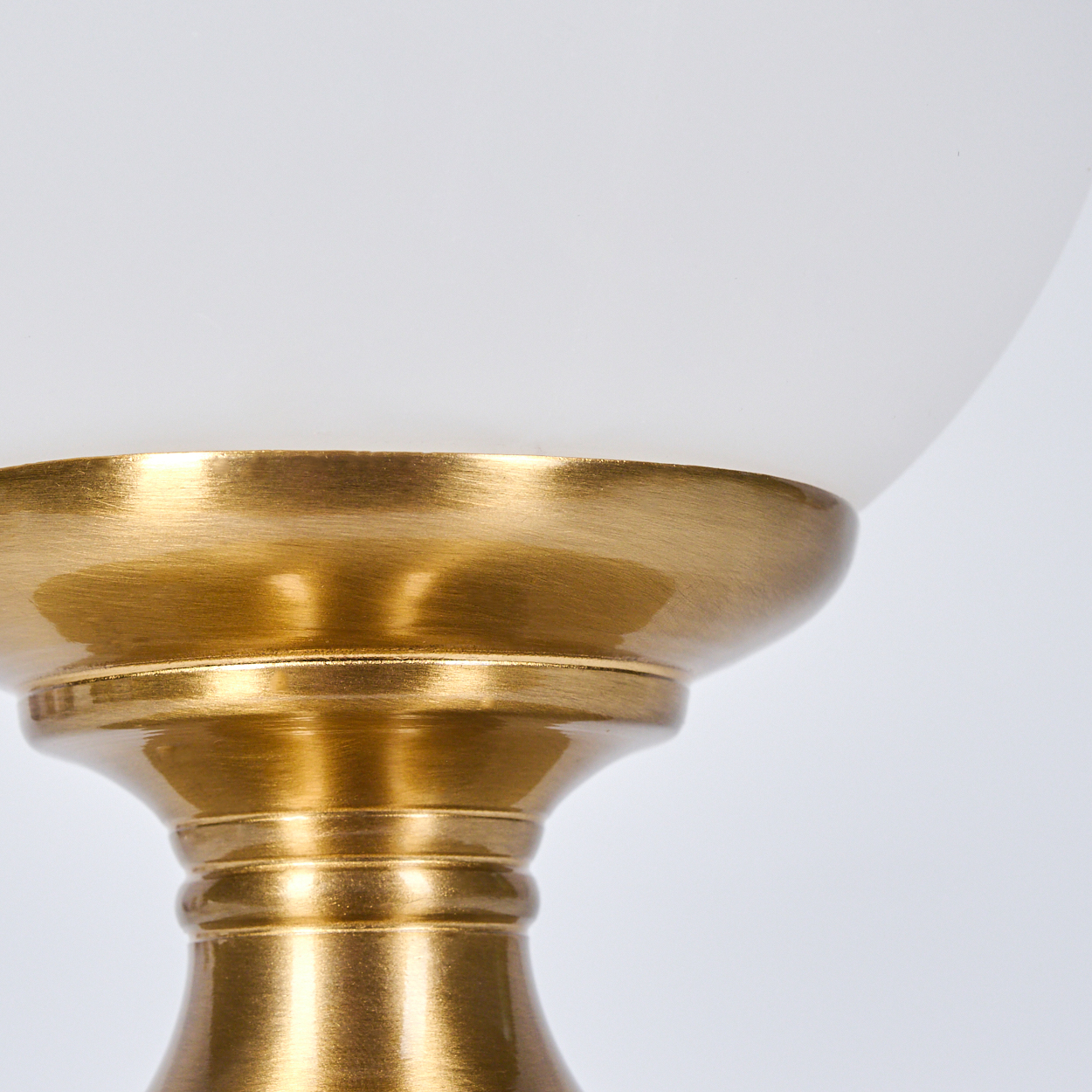 Nahaufnahme eines goldenen Lampensockels mit einer weißen Glaskugel. Der Sockel ist verziert und der Hintergrund ist weiß.