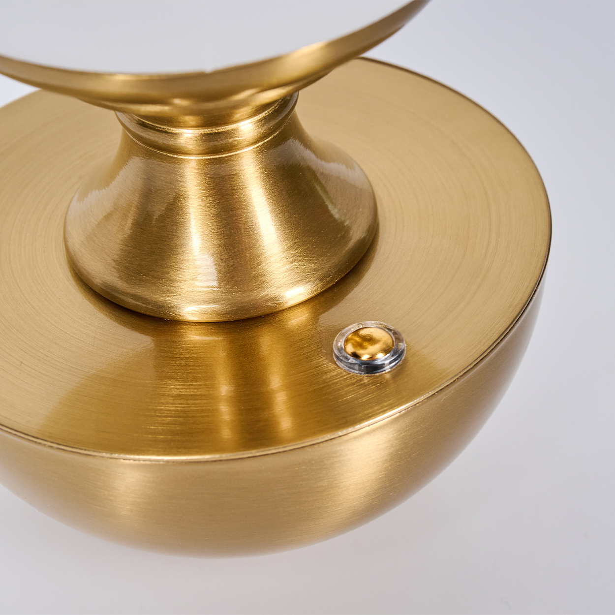Nahaufnahme eines goldenen Lampenfußes mit Knopf. Die Basis ist rund und hat eine gebürstete Metalloberfläche. Der Hintergrund ist weiß.