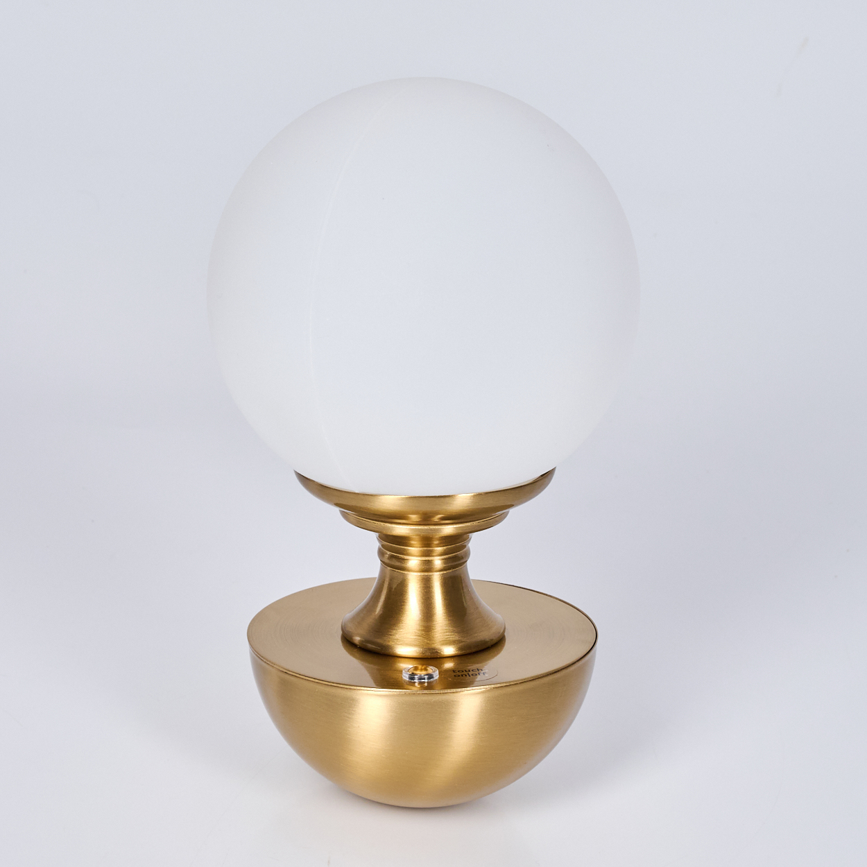 Eine goldfarbene Tischlampe mit kugelförmigem, weißem Glasschirm. Sie hat einen Messingfuß und -schaft, alles vor weißem Hintergrund.