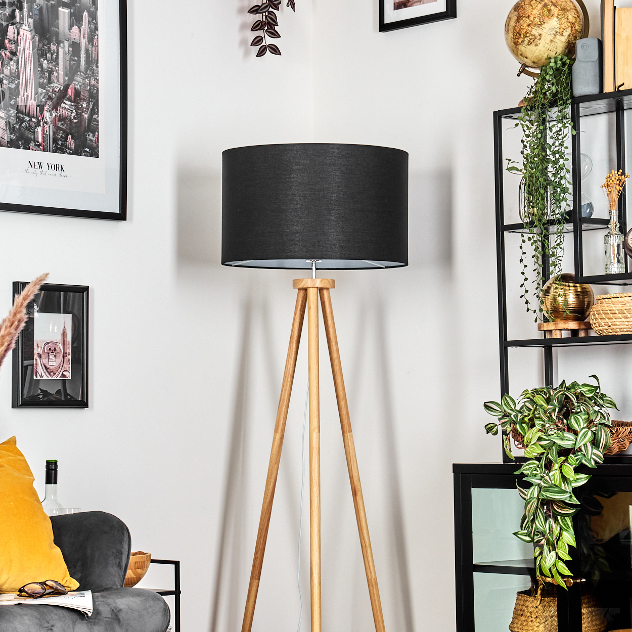 Ein Raum mit einer schwarzen Lampe, Holzbeinen und einem schwarzen Lampenschirm. Es gibt ein New York-Bild und ein Regal mit Pflanzen.