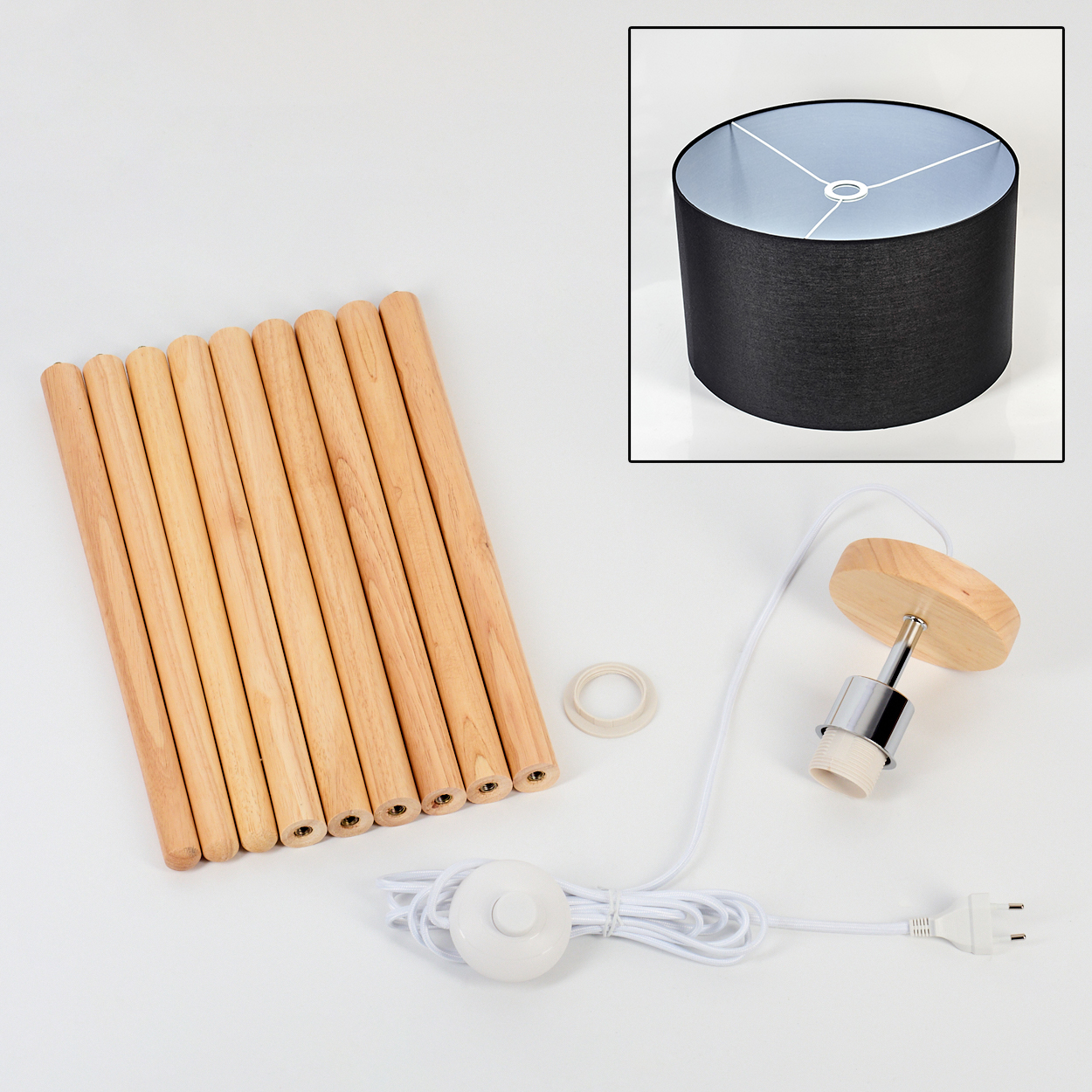 Unmontierte Lampenkomponenten: Holzstäbe, schwarzer Lampenschirm, Leuchte, Schalter, Stecker und ein Ring auf weißer Oberfläche.
