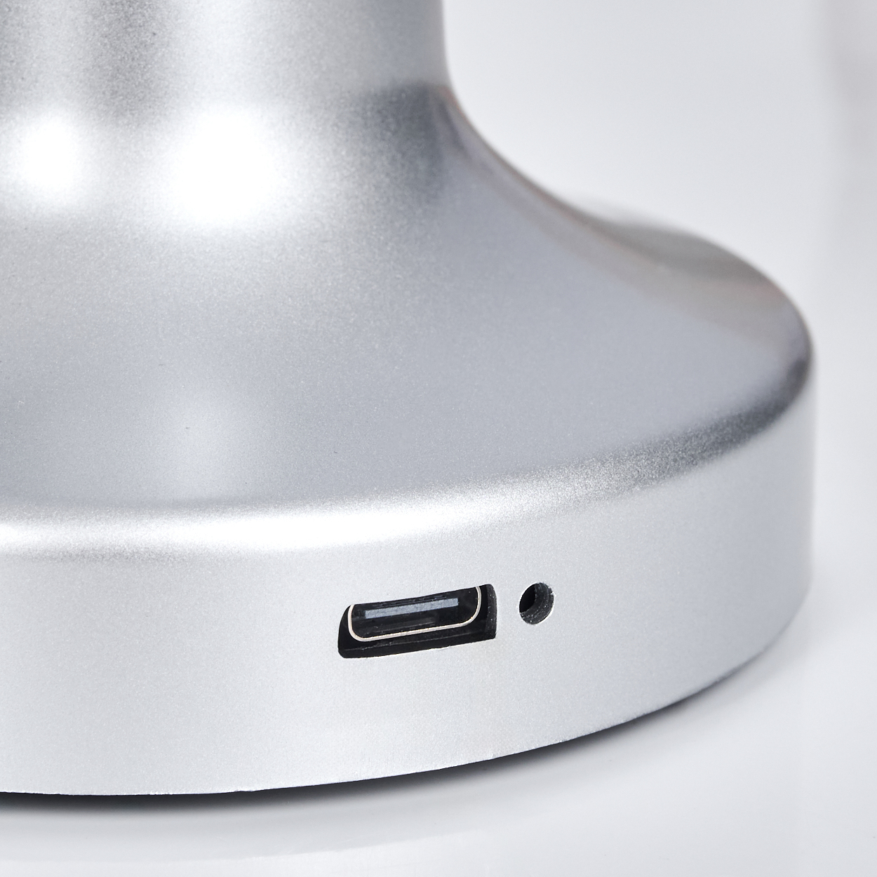 Nahaufnahme eines silbernen Gerätebodens mit USB-Anschluss und einem kleinen Loch. Der Hintergrund ist weiß.