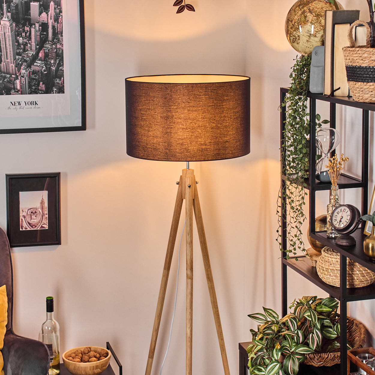 Eine Stehlampe mit Holzstativ und schwarzem Lampenschirm steht in einem Raum mit Bücherregal, New York-Poster und gerahmtem Foto.