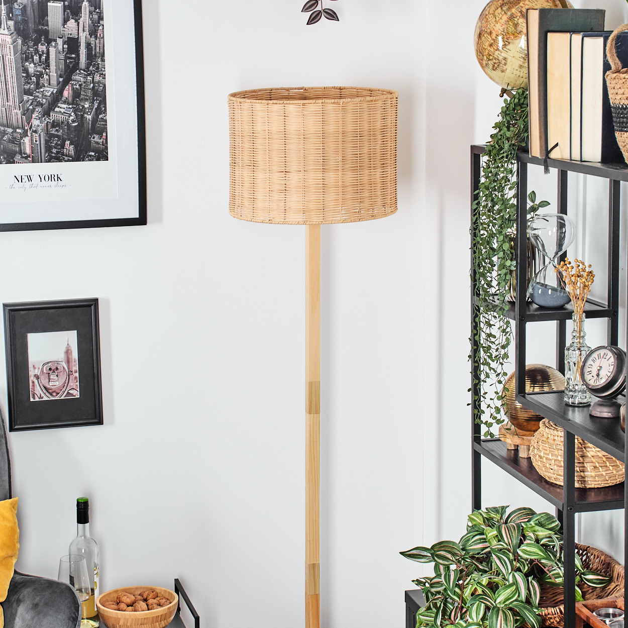 Ein Lampenschirm aus Korbgeflecht steht hoch. Ein New York Stadtbild-Druck hängt an der Wand. Regale mit Dekoration und Pflanzen sind sichtbar.