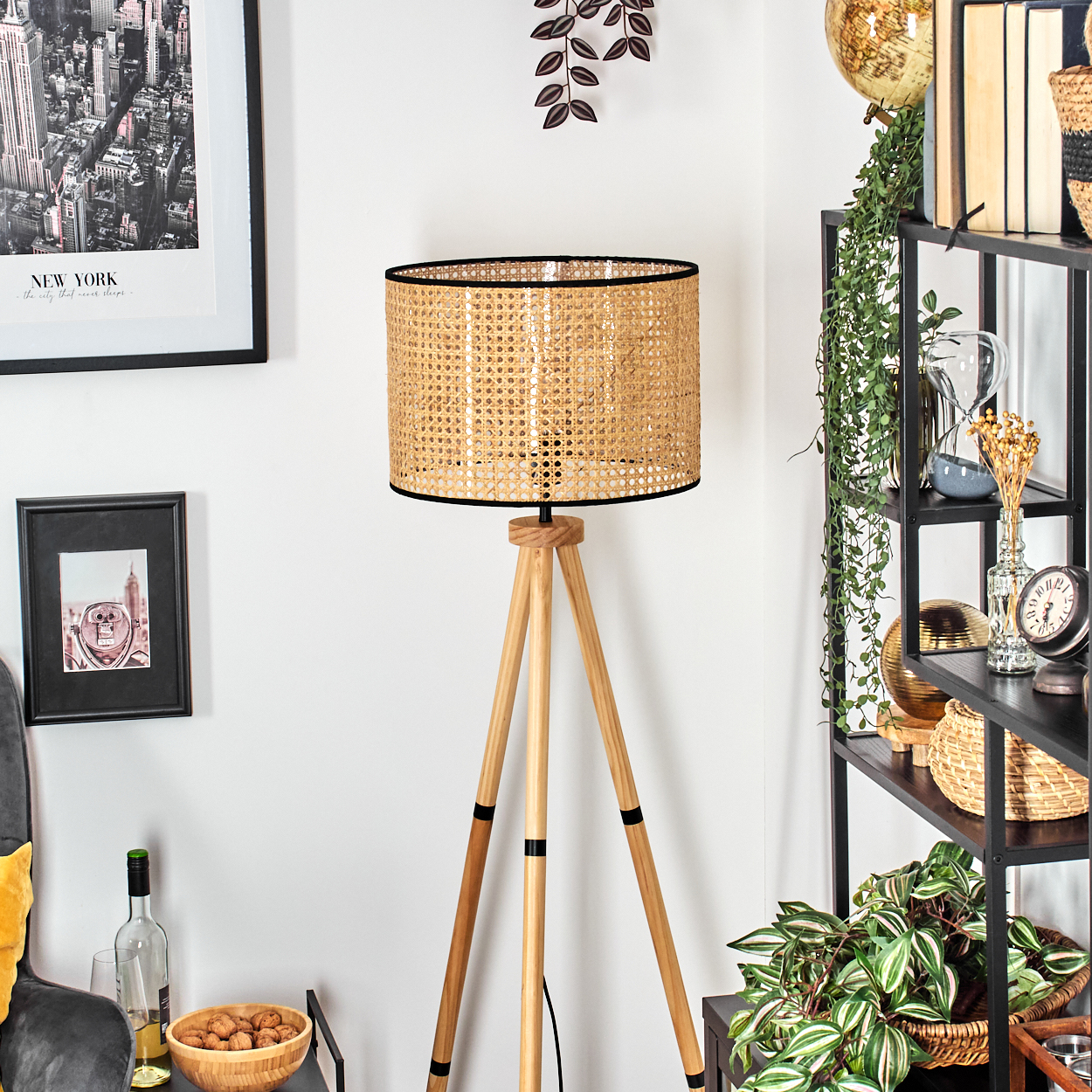 Eine Stehlampe mit gewebtem Lampenschirm steht in einem Raum. Ein Bücherregal und gerahmte Bilder befinden sich im Hintergrund.