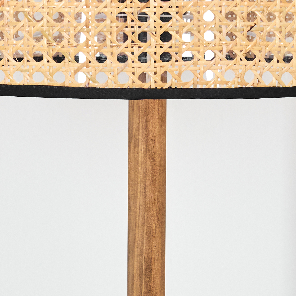 Nahaufnahme einer Lampe. Die Lampe hat einen gewebten Korbschirm mit schwarzem Rand. Der Sockel ist ein Holzpfahl.