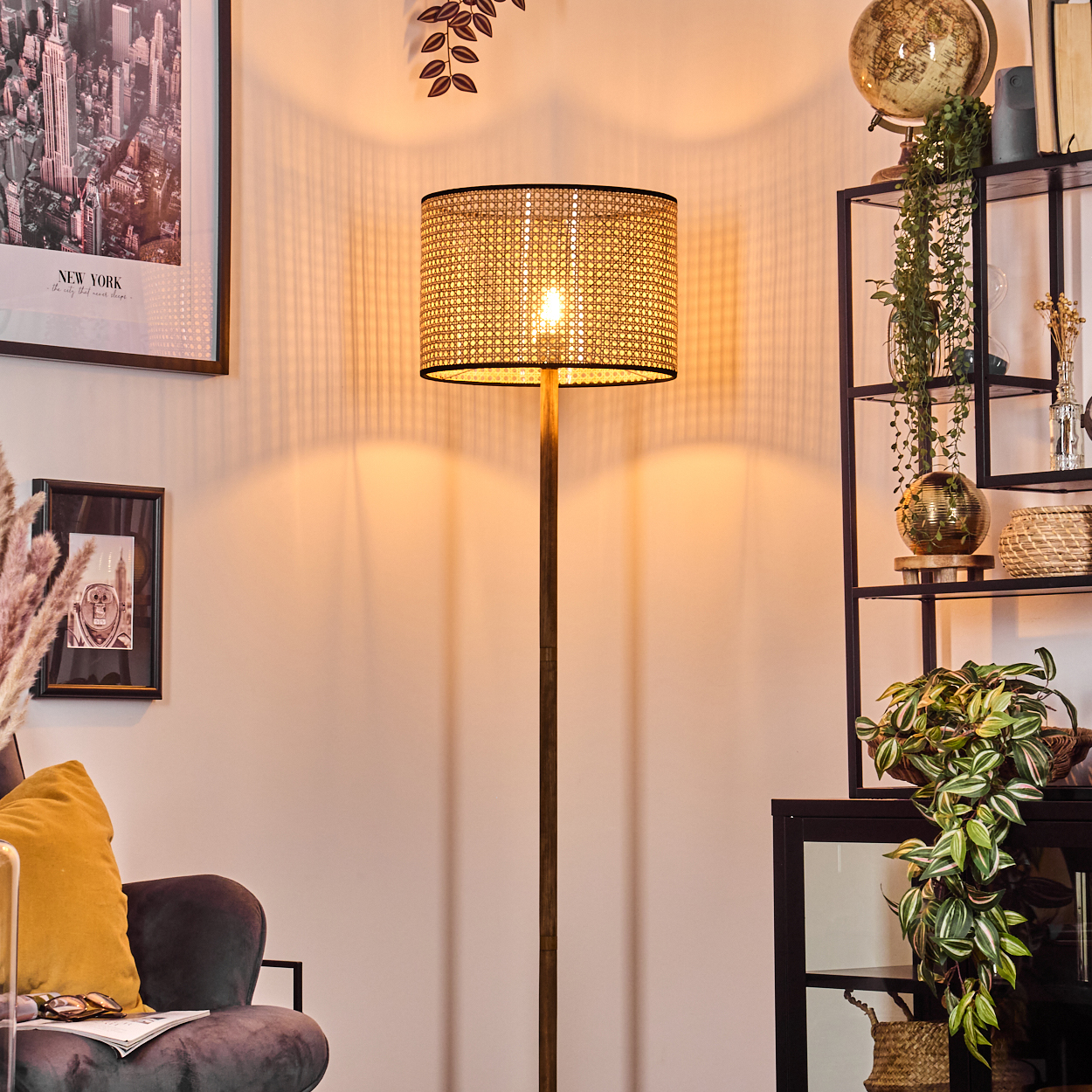 Eine beleuchtete Lampe steht in einem Raum. Ein gerahmtes Bild von New York hängt an der Wand. Regale mit Pflanzen und Dekoration.
