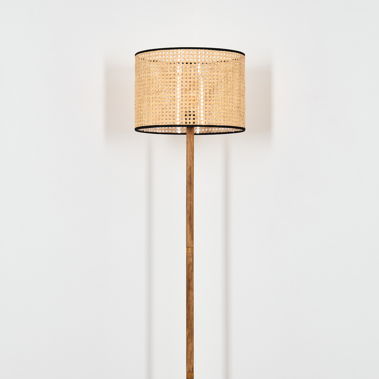 Eine Stehlampe mit gewebtem Lampenschirm und Holzständer. Der Lampenschirm ist hellbeige, der Ständer braun.