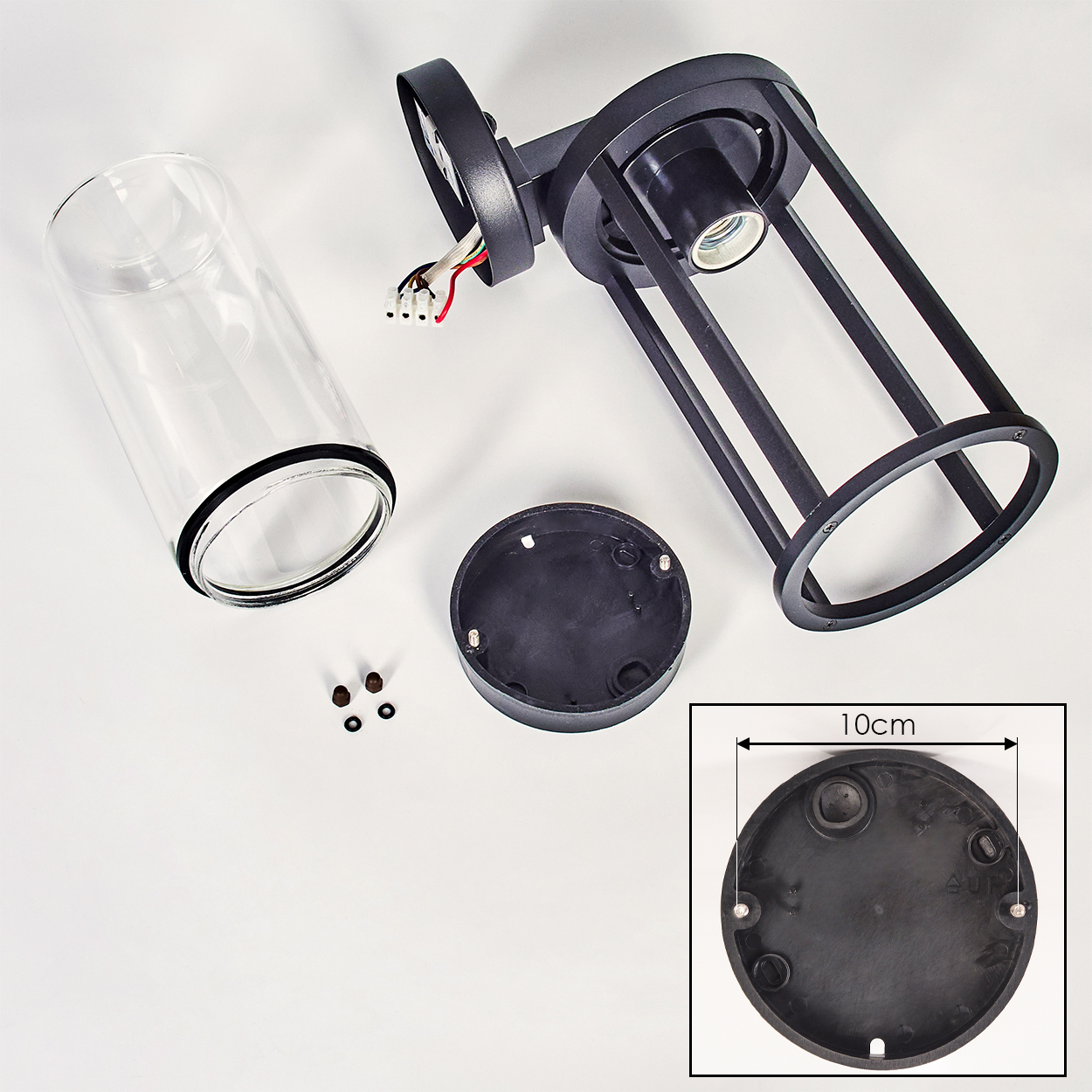 Zerlegte schwarze Außenleuchte mit Glaszylinder, Sockel und Kleinteilen auf weißer Oberfläche. Ein 10 cm großer Sockel ist abgebildet.