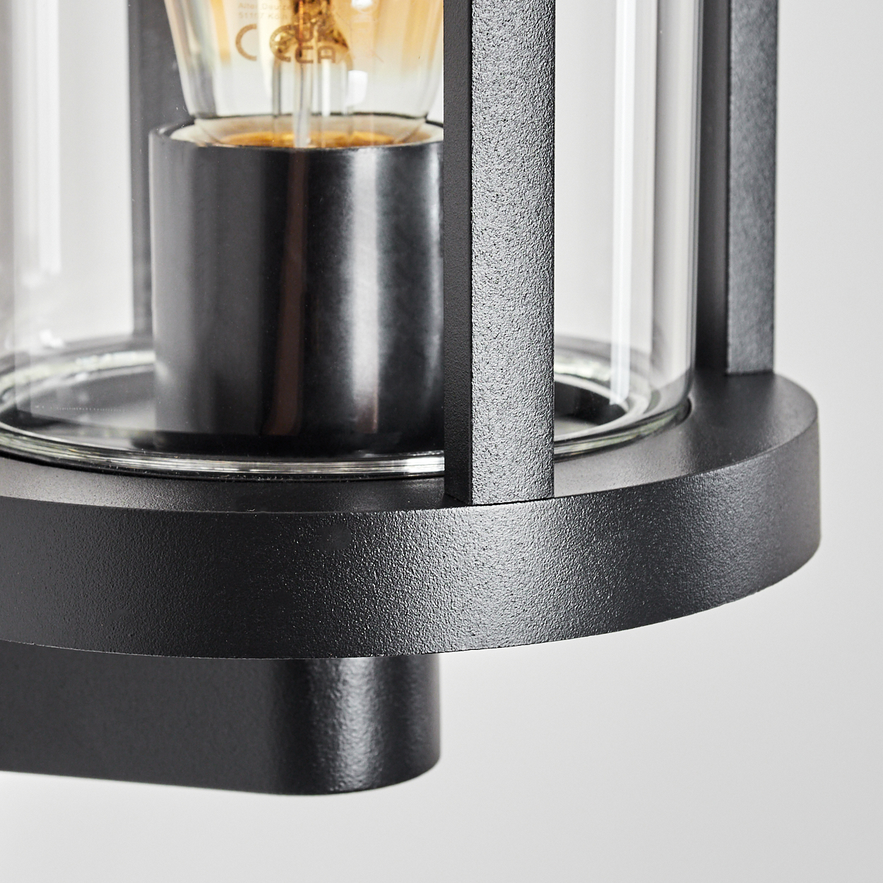 Nahaufnahme einer schwarzen Außenlampe. Sie hat einen Glaskolben und eine Glühbirne. Der Hintergrund ist schlicht weiß.