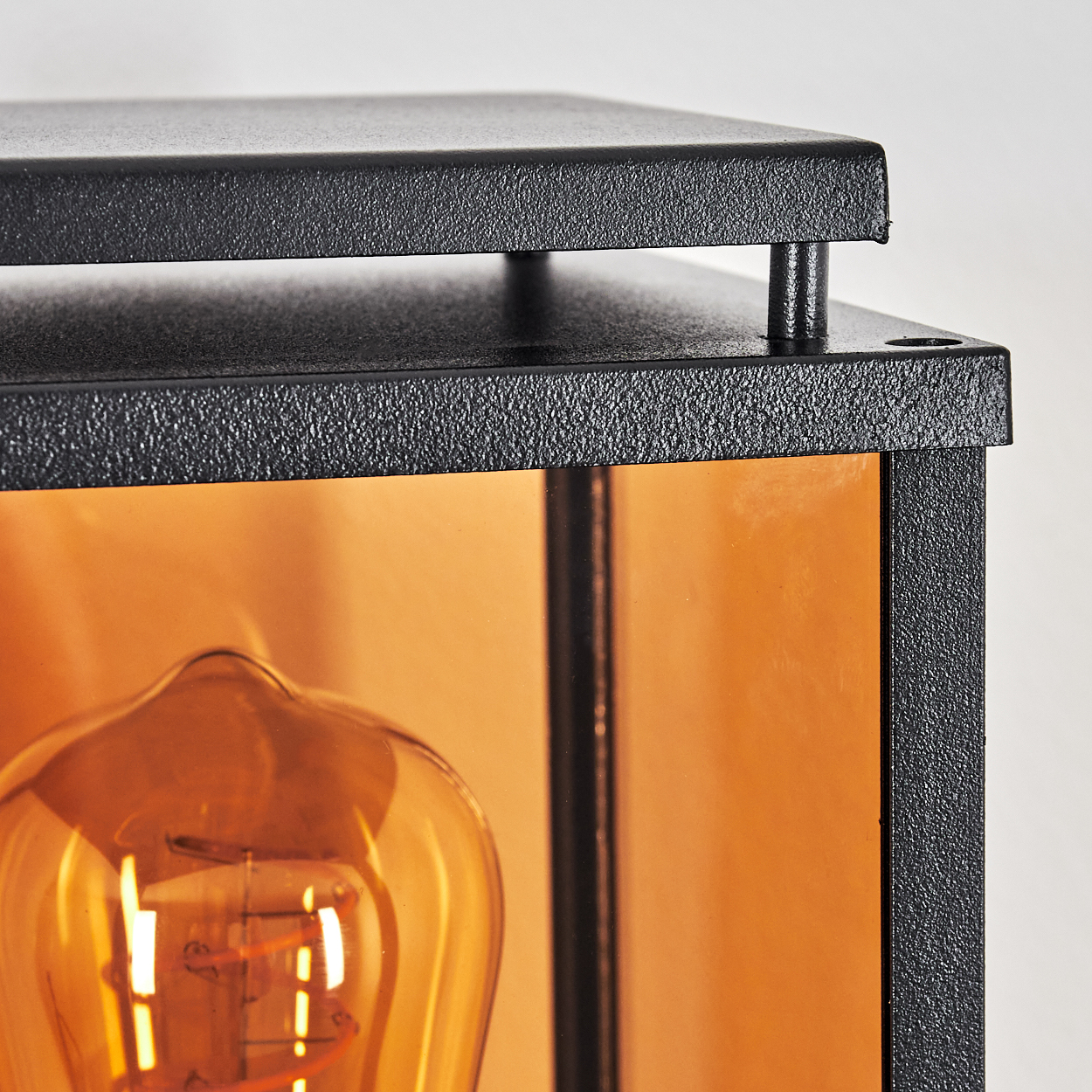 Nahaufnahme einer schwarzen Metalllampe. Sichtbar ist eine warmtonige Glühbirne in einem bernsteinfarbenen Glasgehäuse.