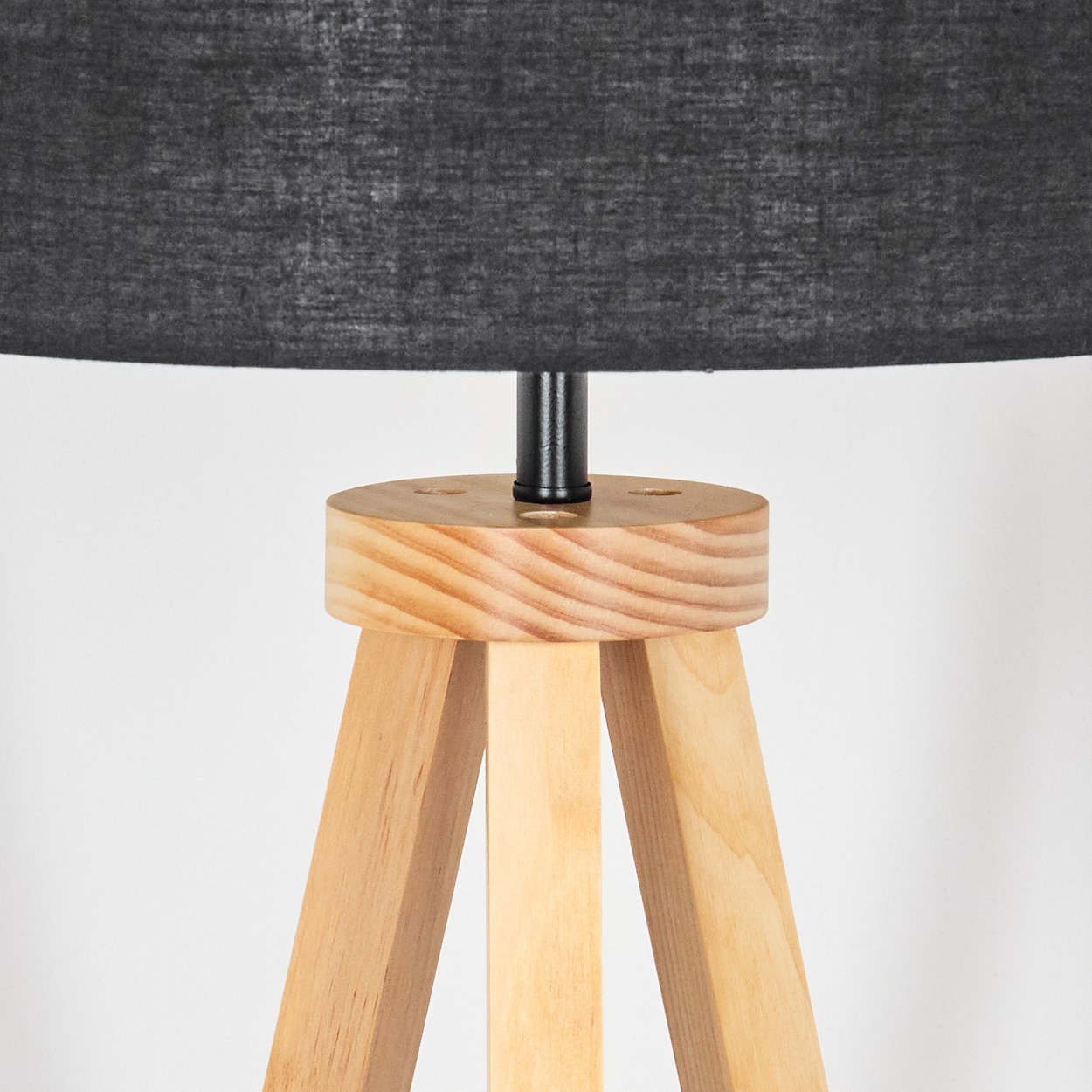 Eine Lampe mit schwarzem Lampenschirm steht auf einem hölzernen Stativfuß. Die Lampe steht vor einem weißen Hintergrund.